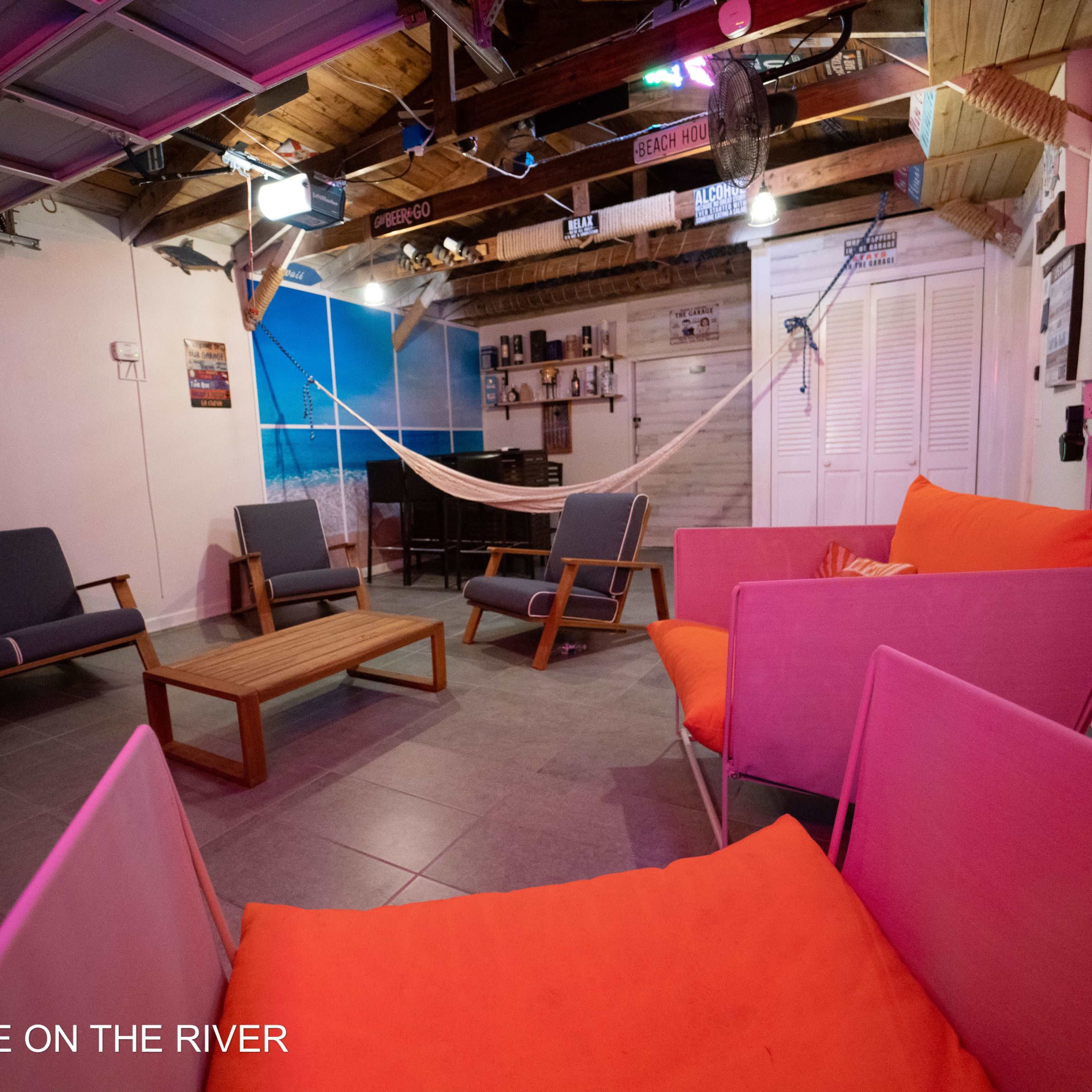 A casual lounge area with gray and pink seating, a wooden coffee table, and a hammock, set against a backdrop of beach-themed decor.