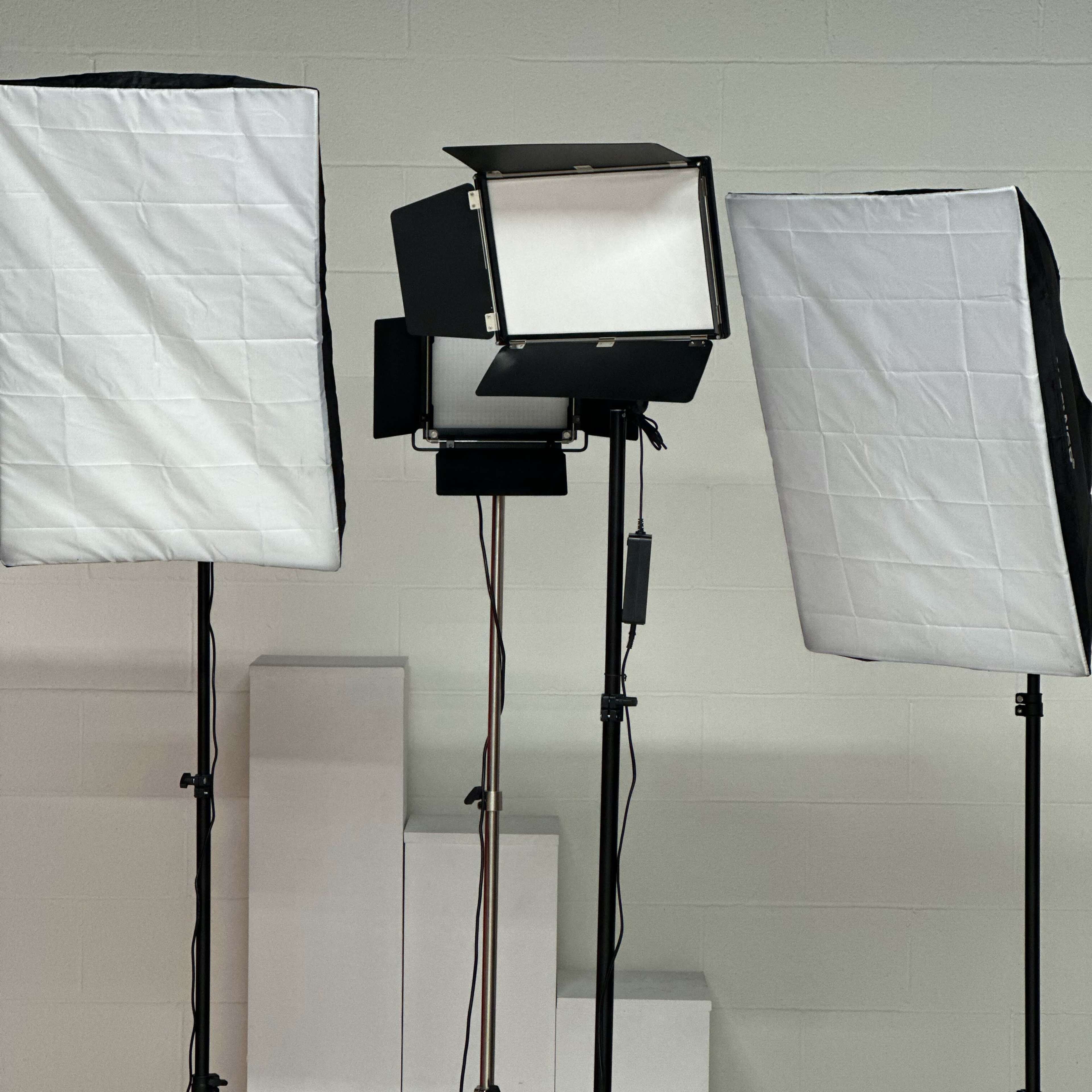Three softbox lights set up on stands, facing a backdrop of white steps against a plain wall.