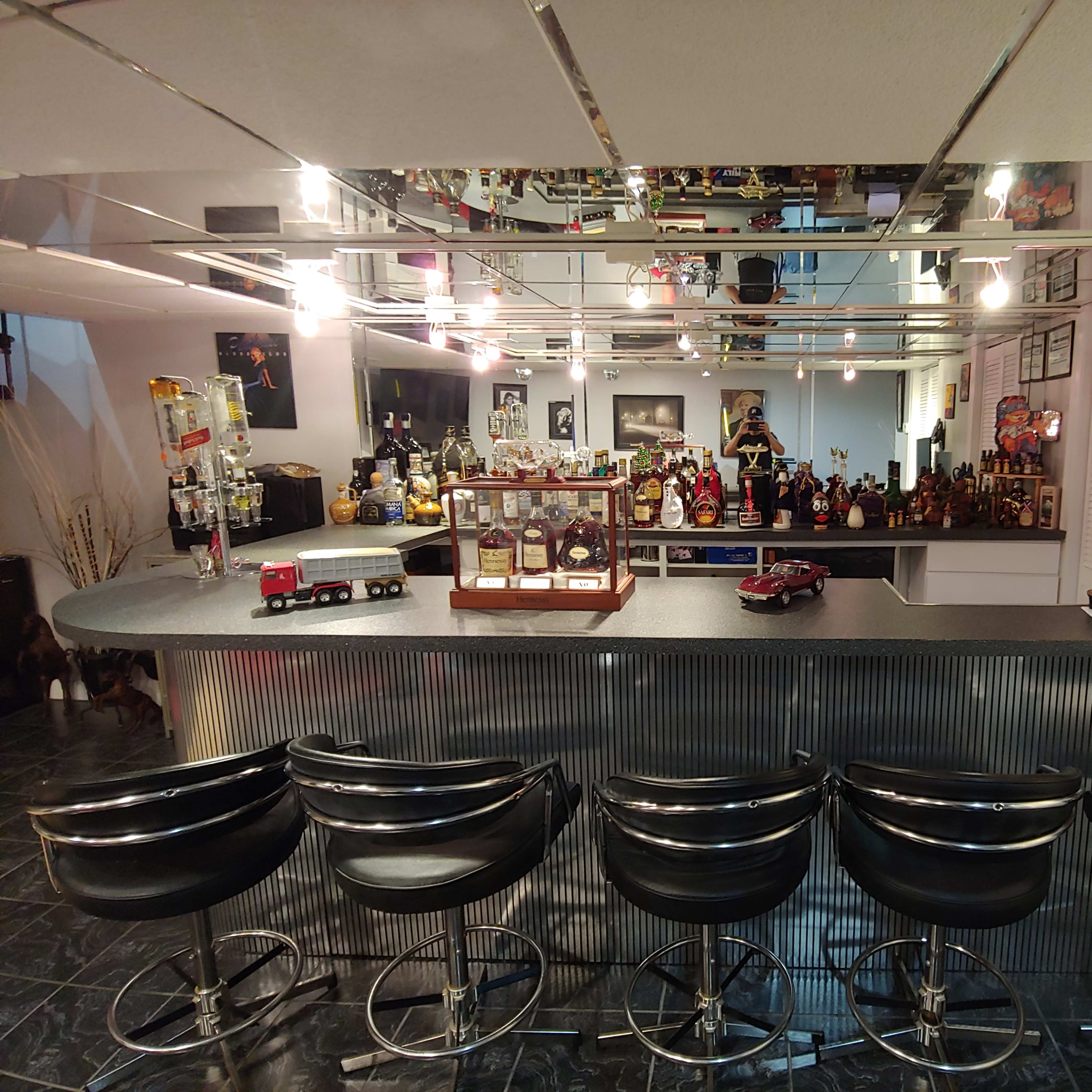 A stylish home bar with a curved counter, bar stools, and a display of various bottles and collectibles.