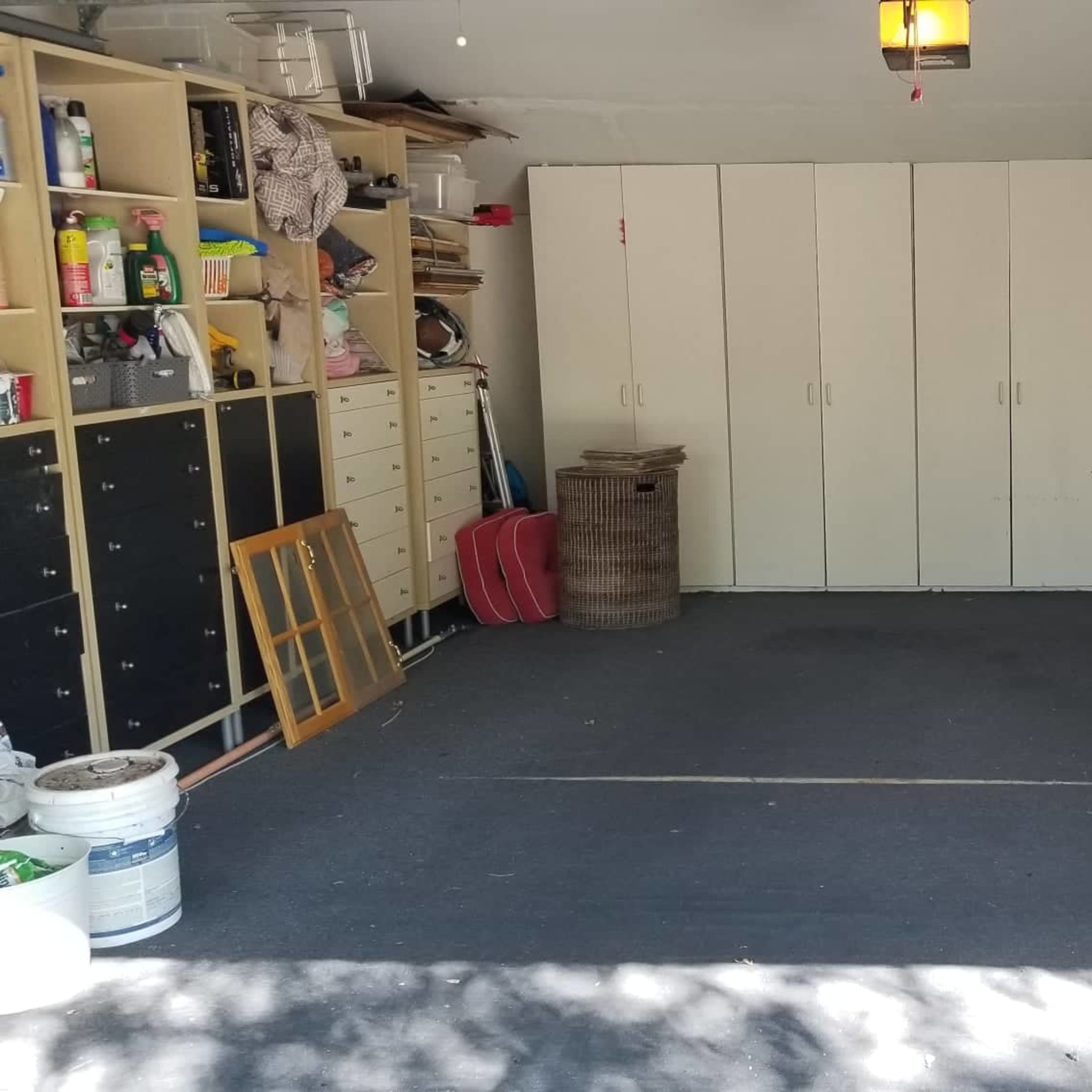 A spacious garage with white cabinets lining one wall and various household items organized on shelves.