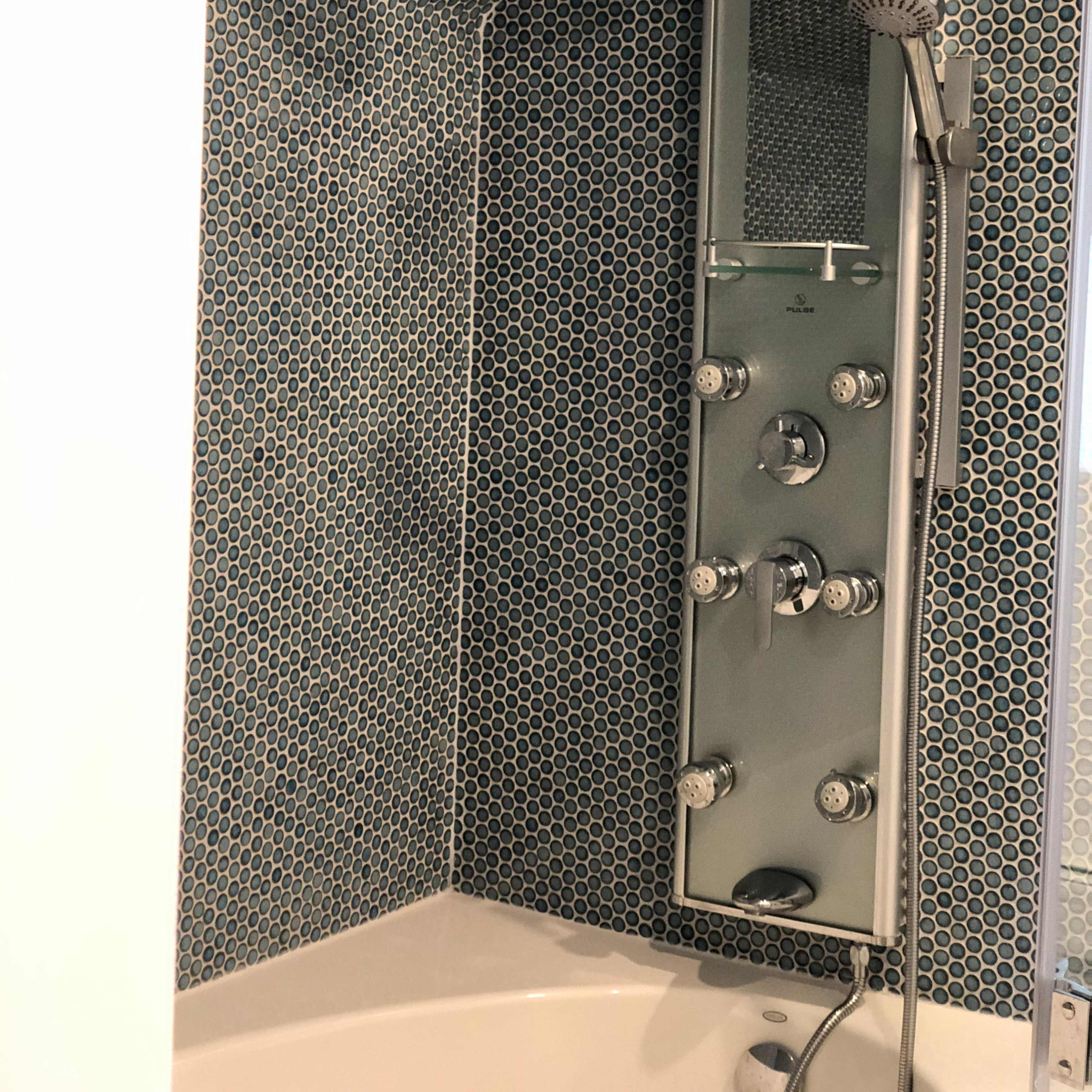A modern shower area featuring a tile wall with a honeycomb pattern and a sleek shower panel with multiple water controls and a handheld showerhead.