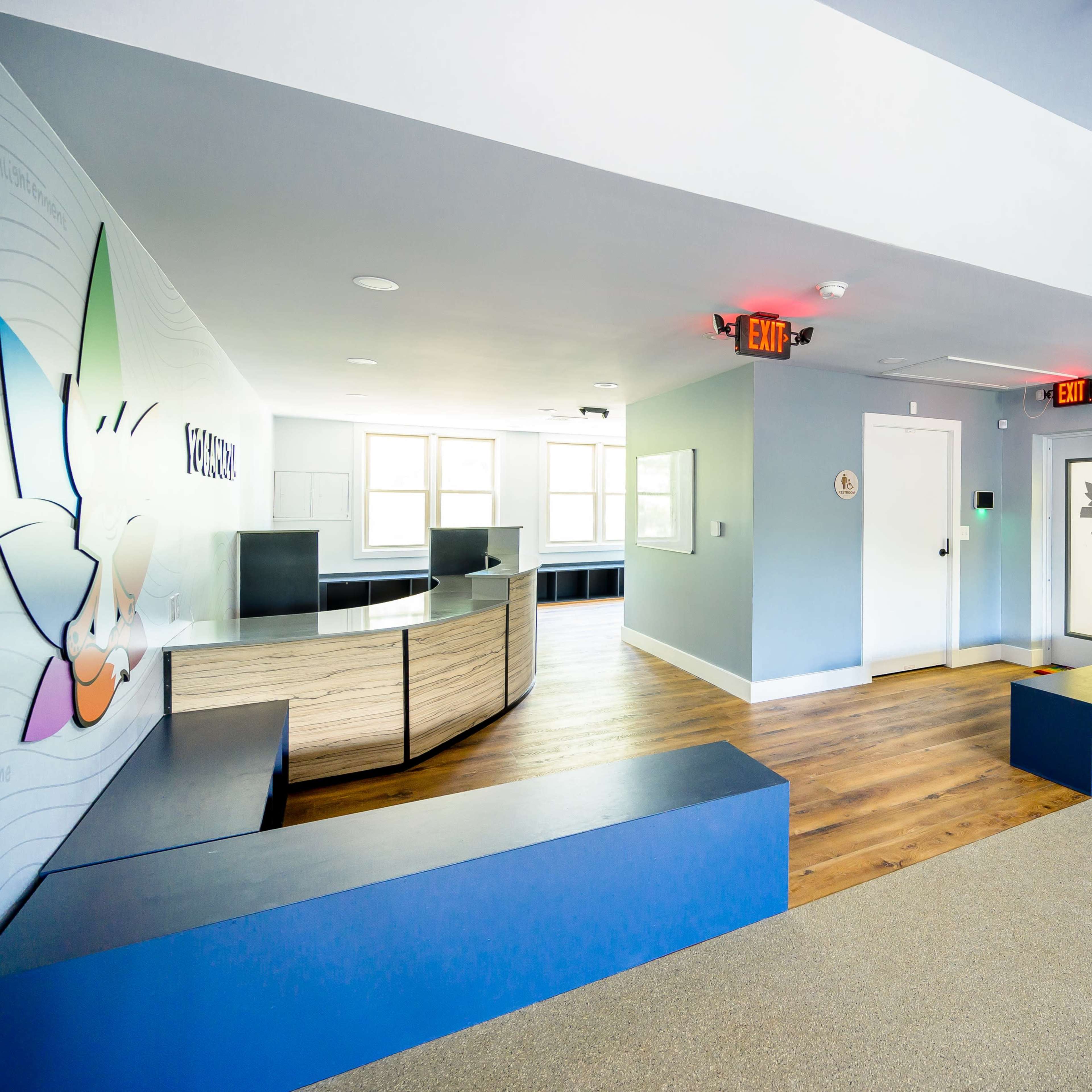 A modern reception area with light blue walls, wooden flooring, and a curved front desk.