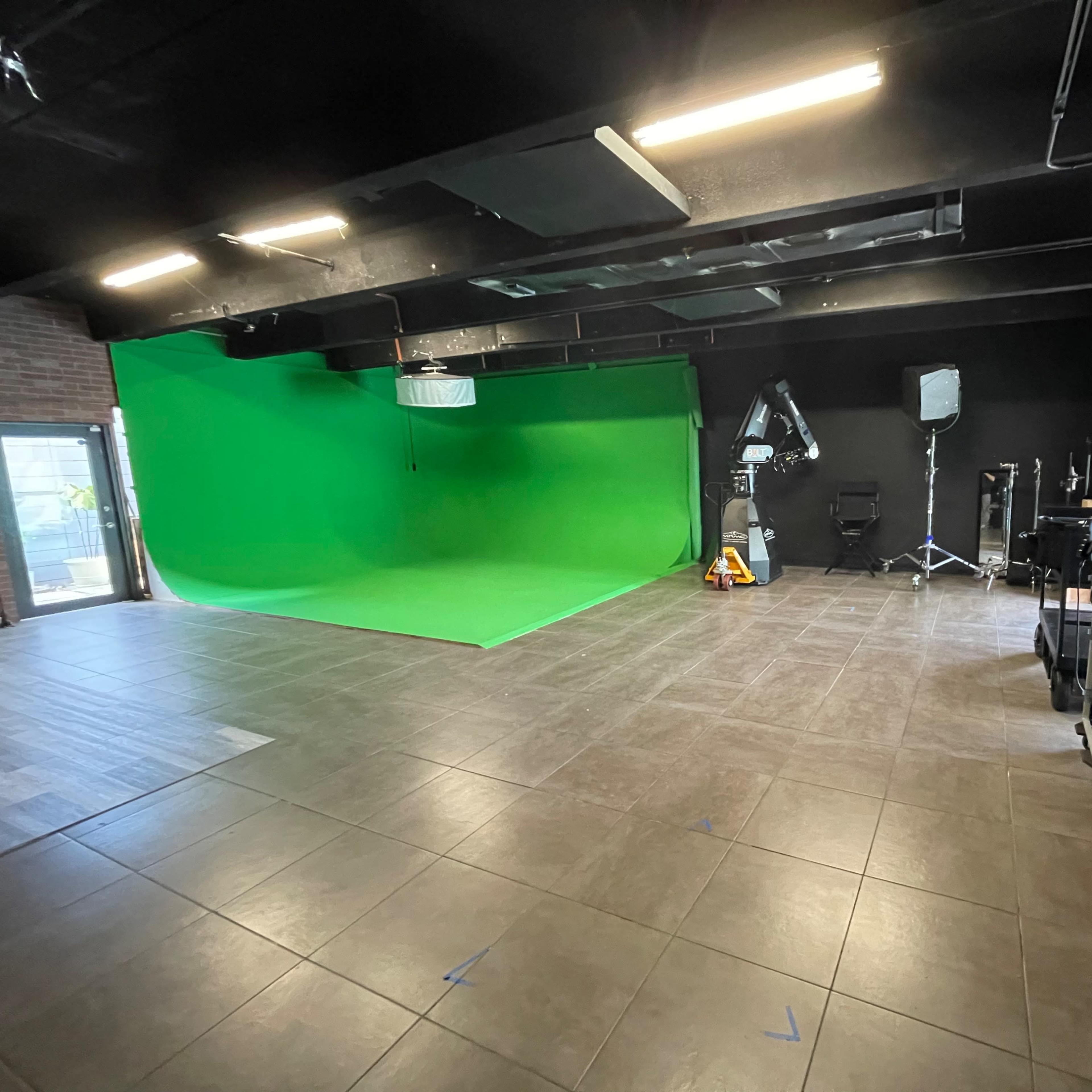 A green screen studio with a bright green backdrop, lighting equipment, and various filming accessories arranged in the space.