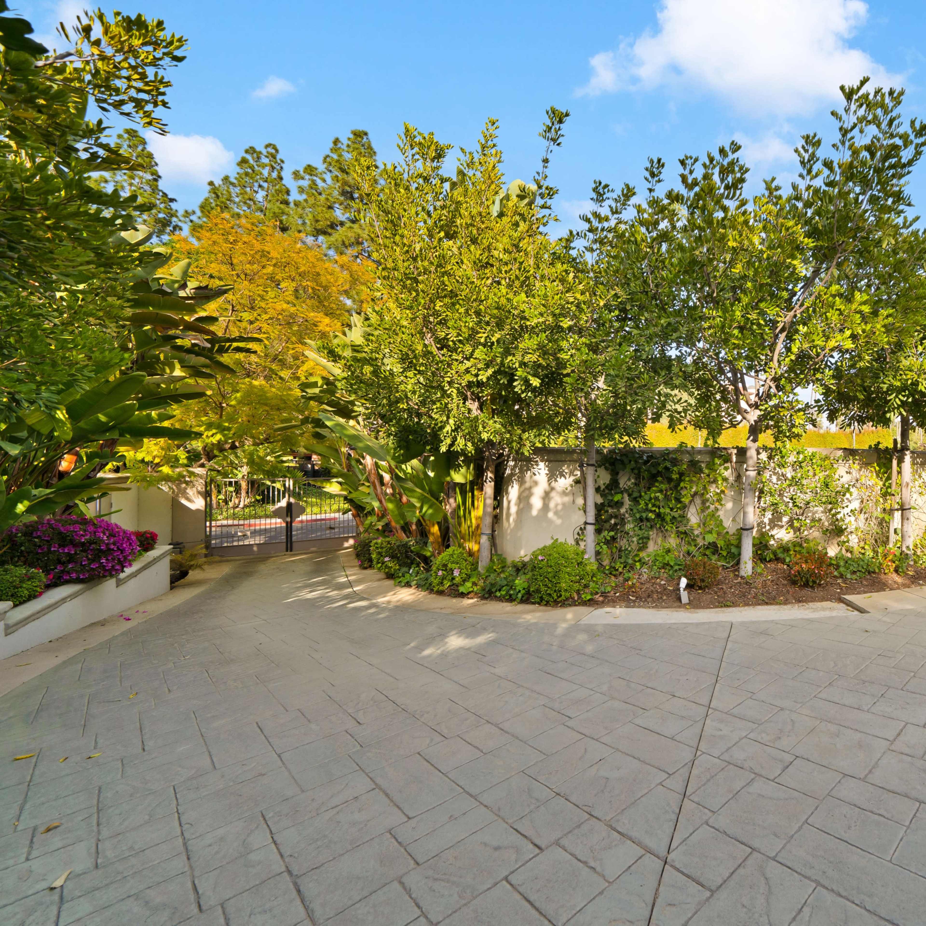 A landscaped driveway curves around a lush garden leading to a gated entrance.