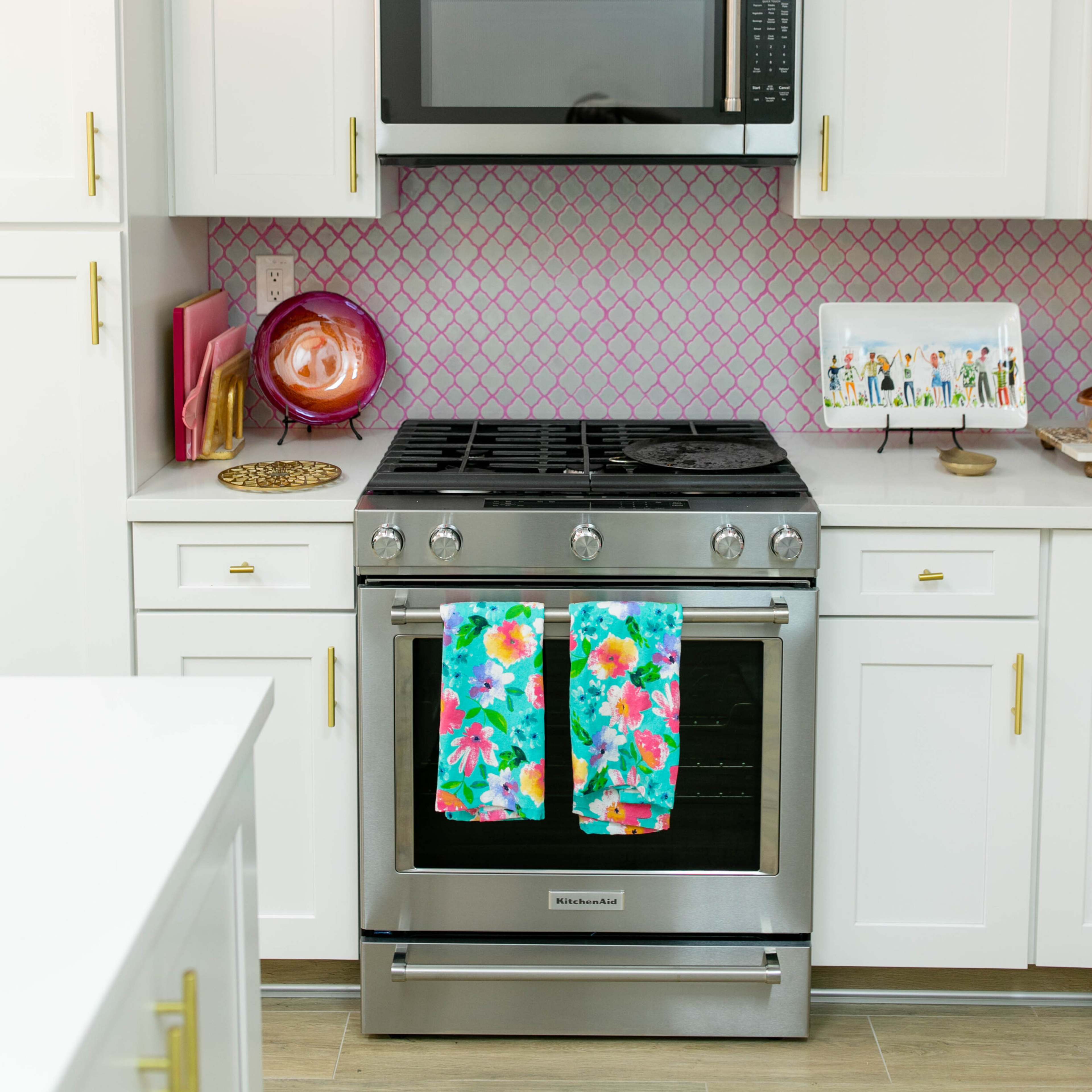 A modern kitchen with white cabinetry, a stainless steel gas range, and a microwave above it, all set against a pink-tiled backsplash.