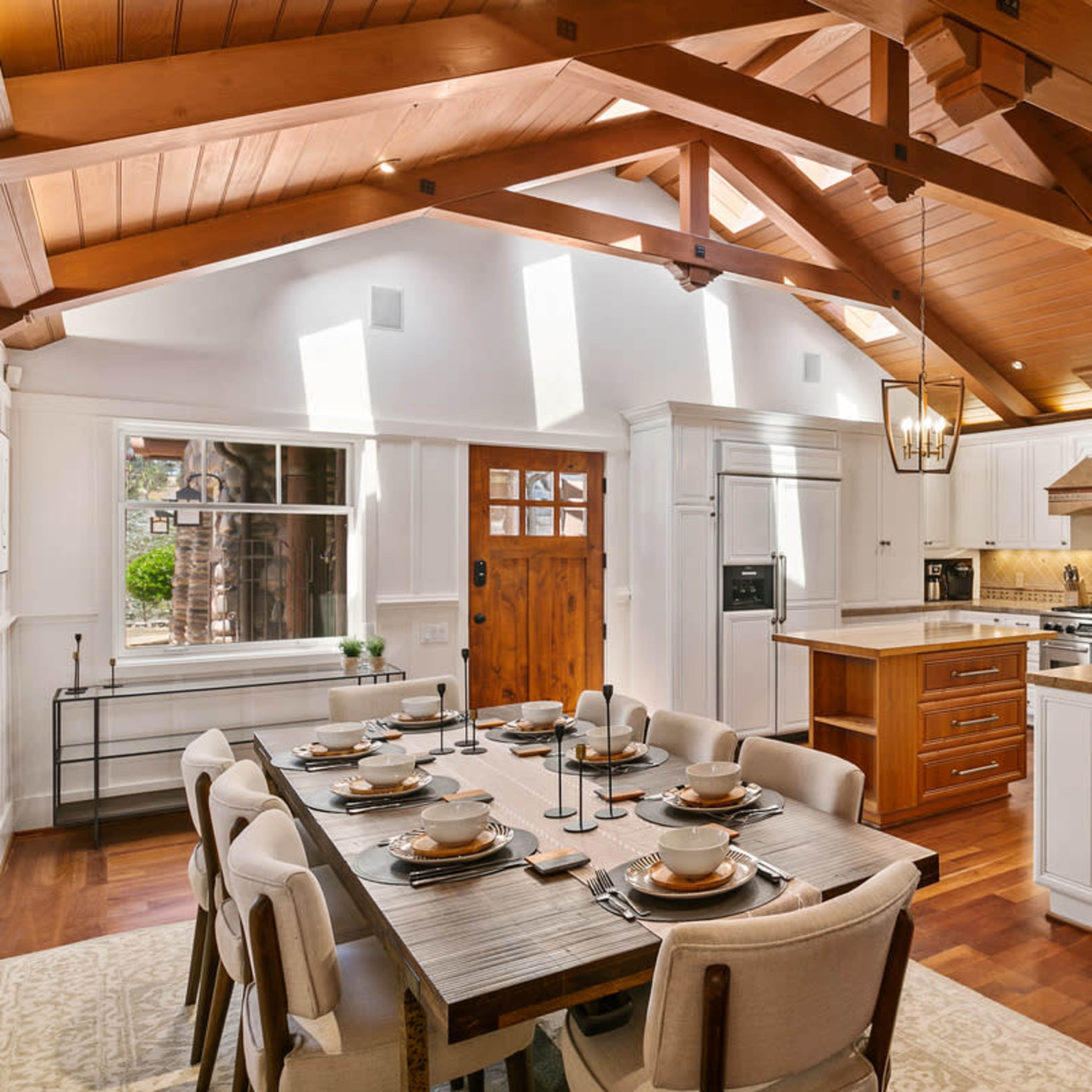 A spacious kitchen with wooden beams, a large dining table set for eight, and a center island with a stove and range hood.
