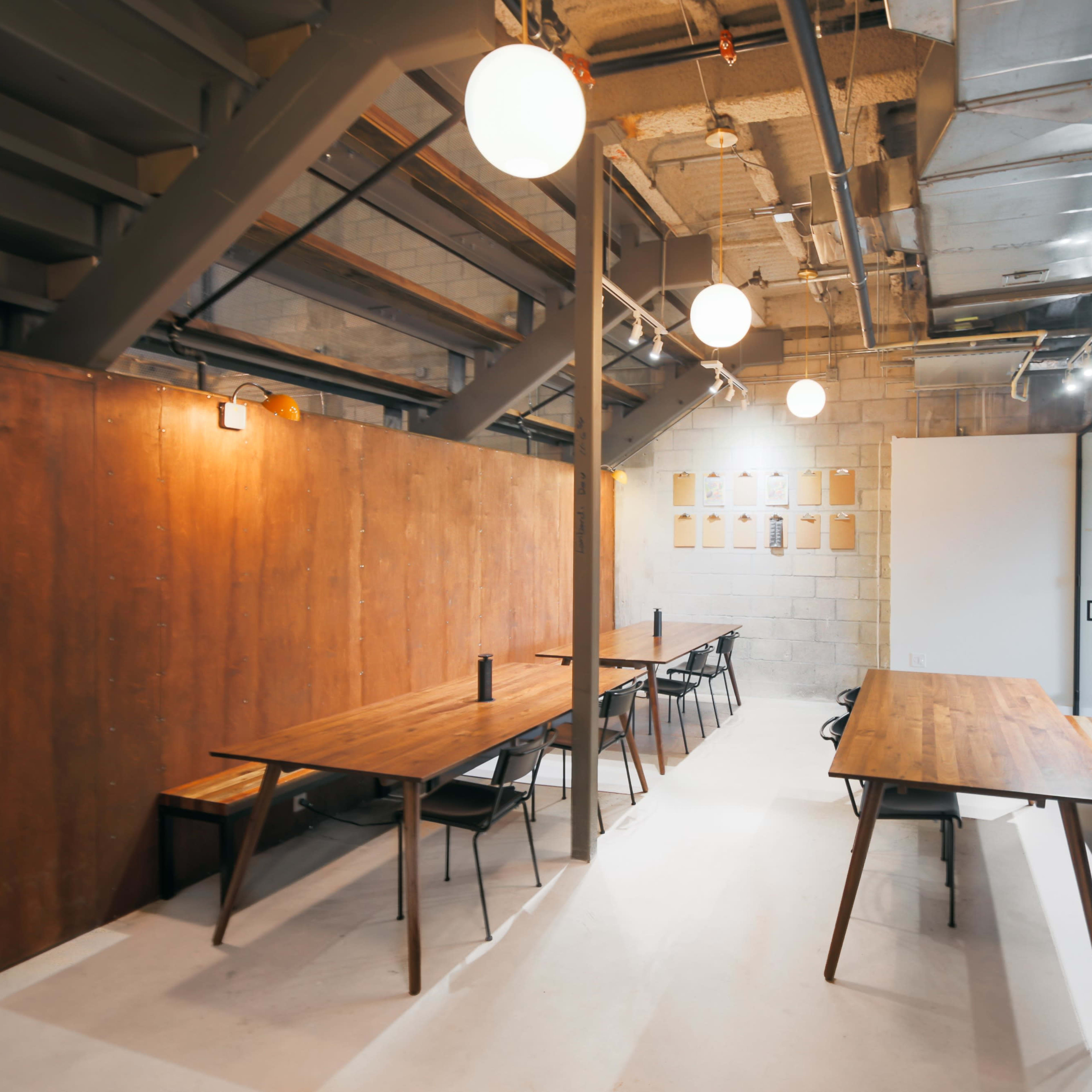 A modern workspace with wooden tables, black chairs, and overhead lighting in an industrial-style interior.