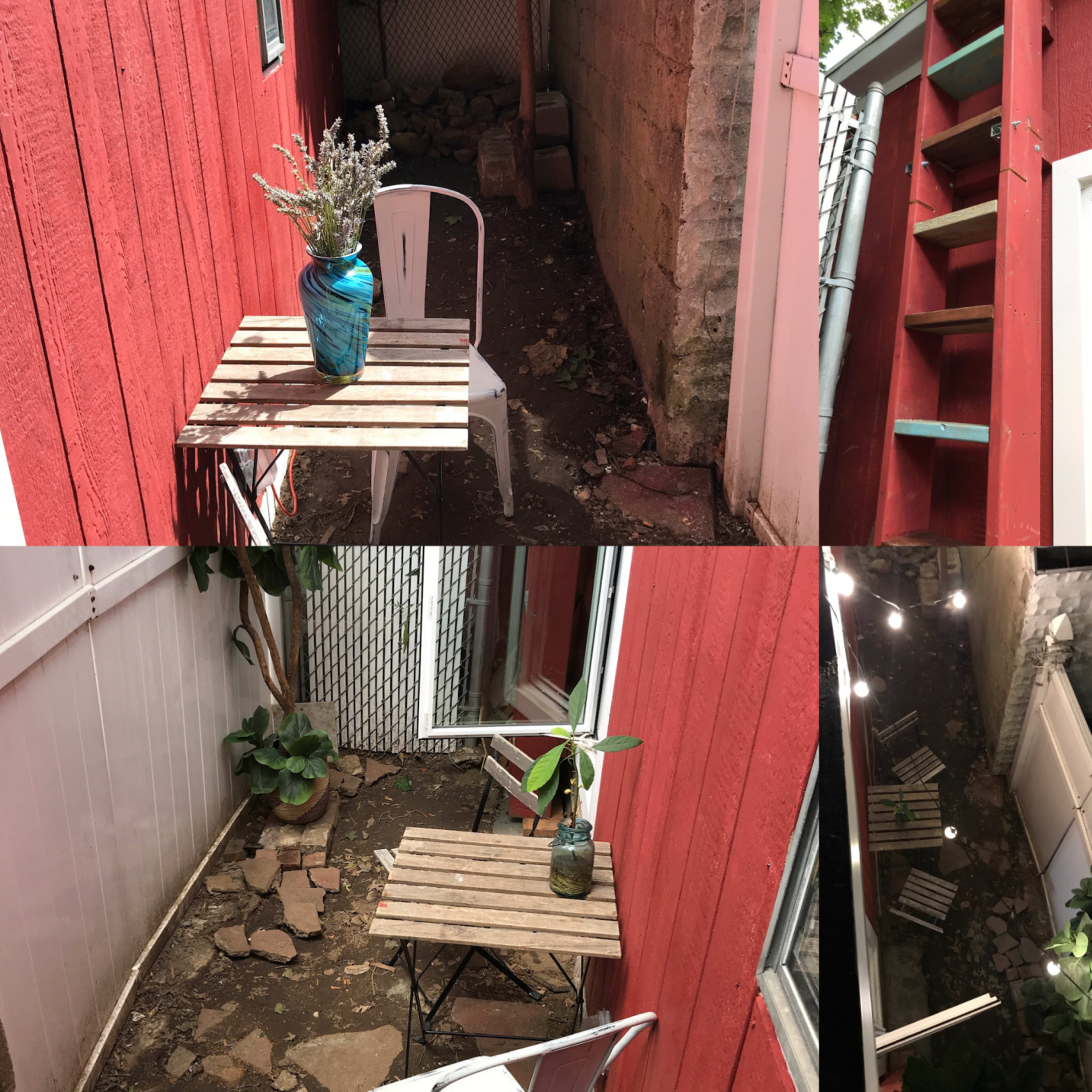 A narrow outdoor space between two red buildings, featuring a small wooden table with a potted plant and a staircase leading to an upper level.