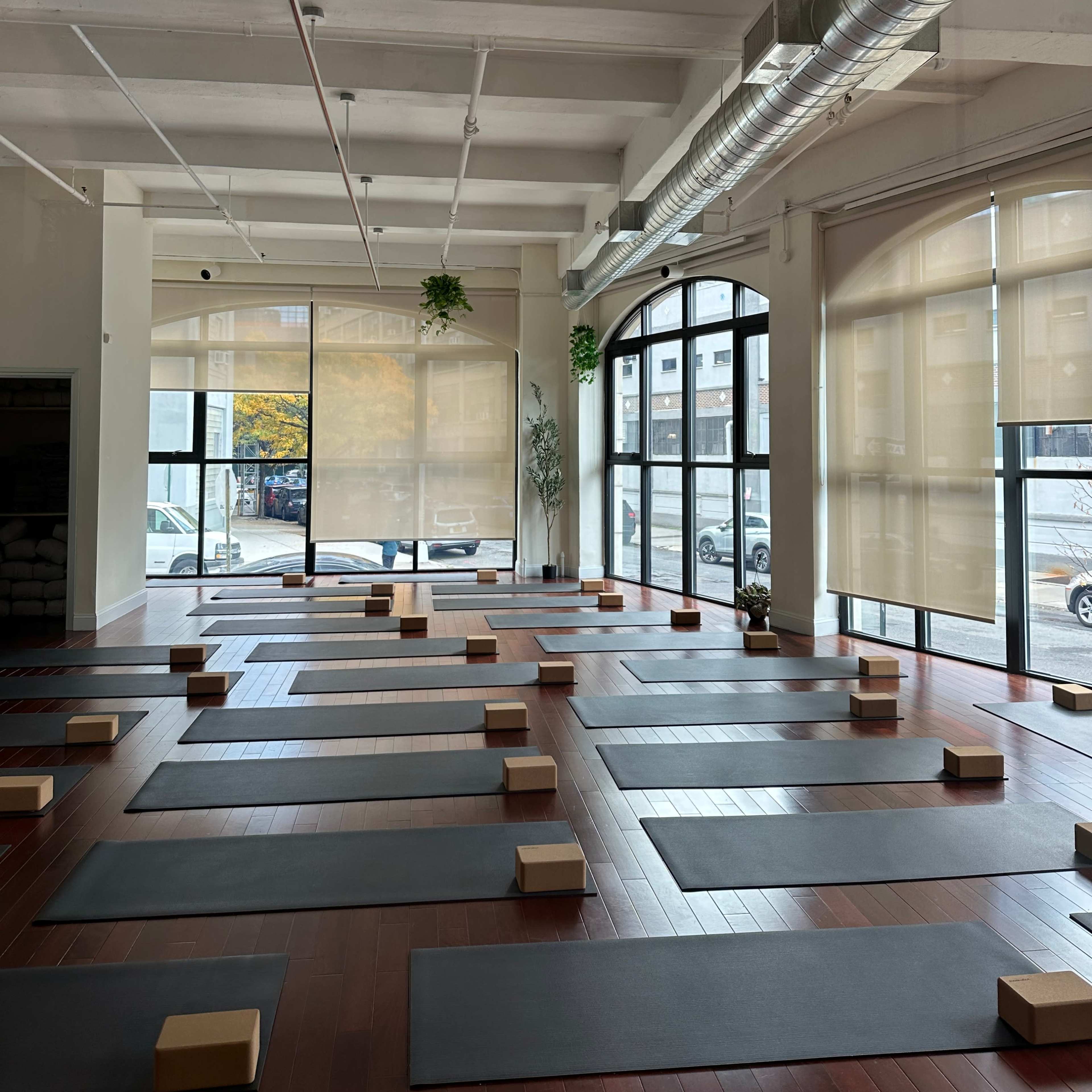 A spacious yoga studio with neatly arranged mats, blocks, and large windows letting in natural light.