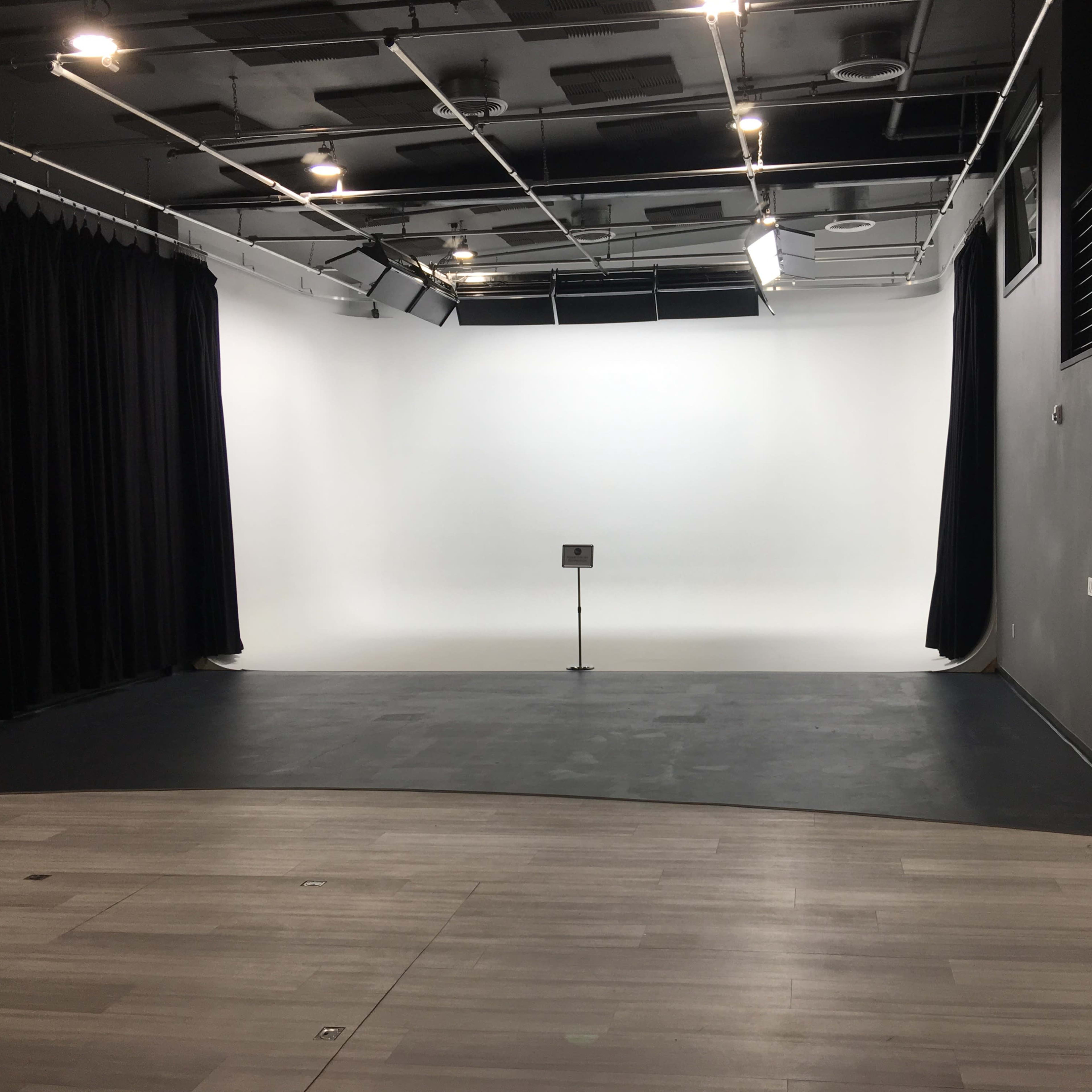 A spacious, empty studio with a white backdrop and a black curtain, featuring a microphone stand in the center.