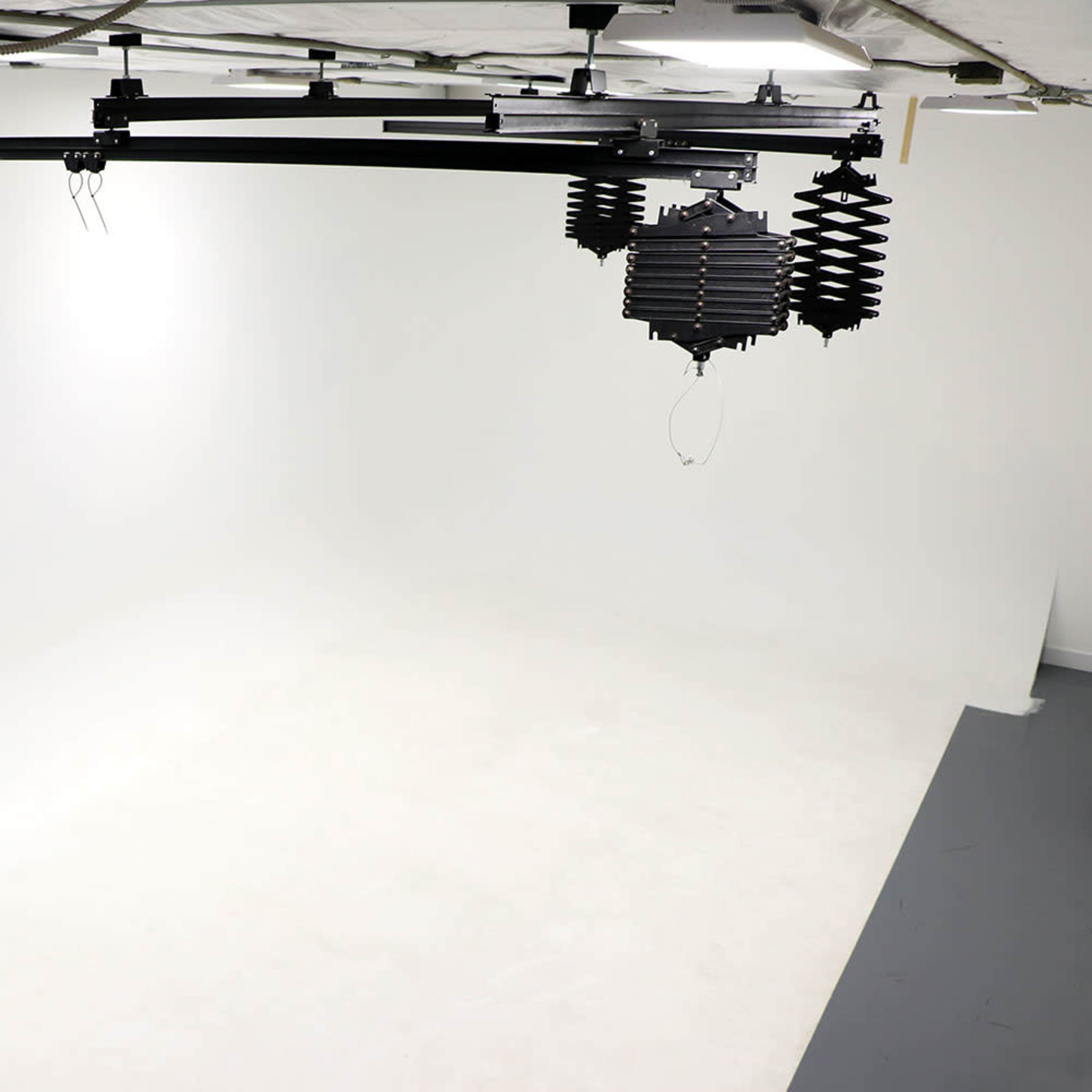 A well-lit photography studio with a seamless white backdrop and overhead lighting fixtures.