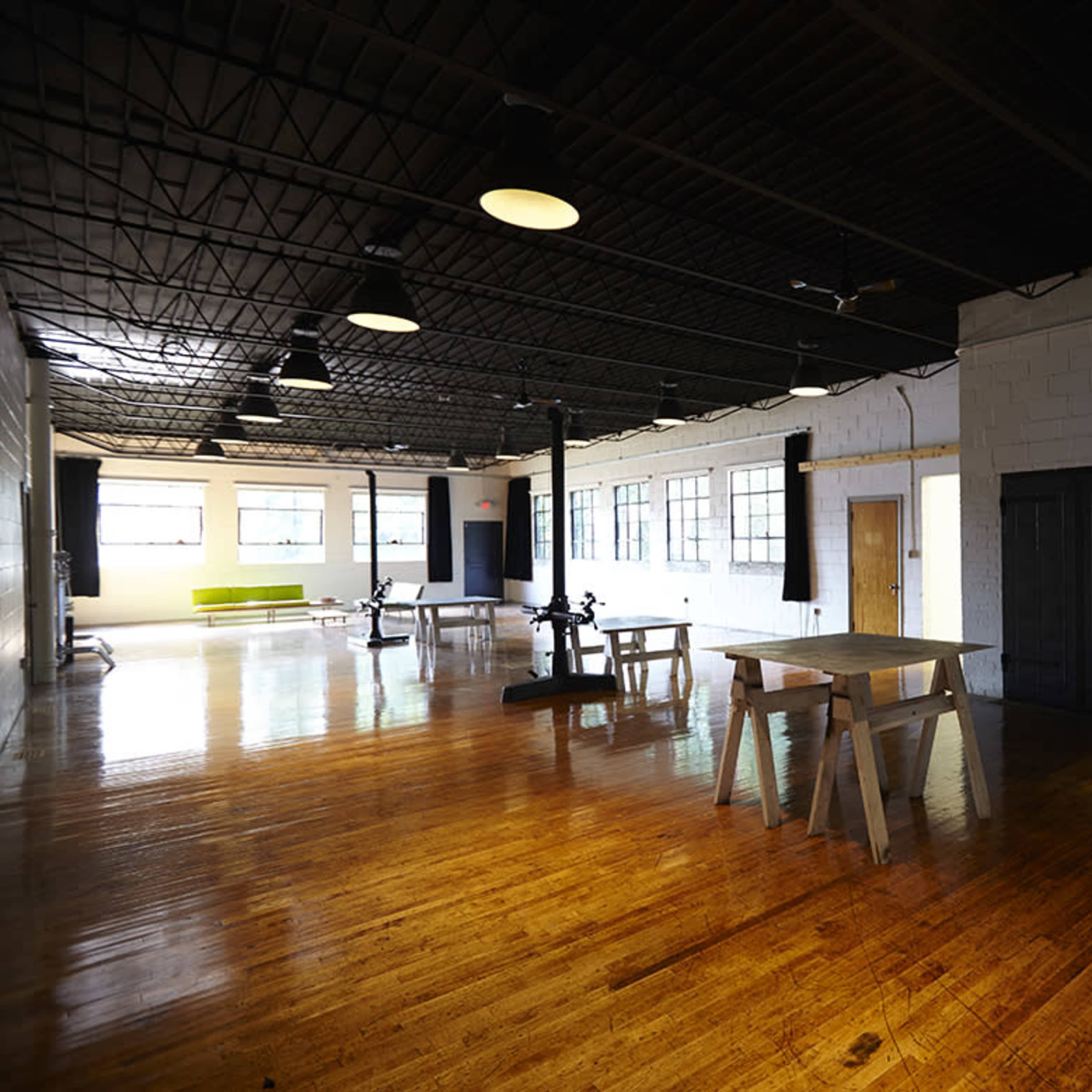 A spacious, empty industrial loft with polished wooden floors, large windows, and minimal furniture.