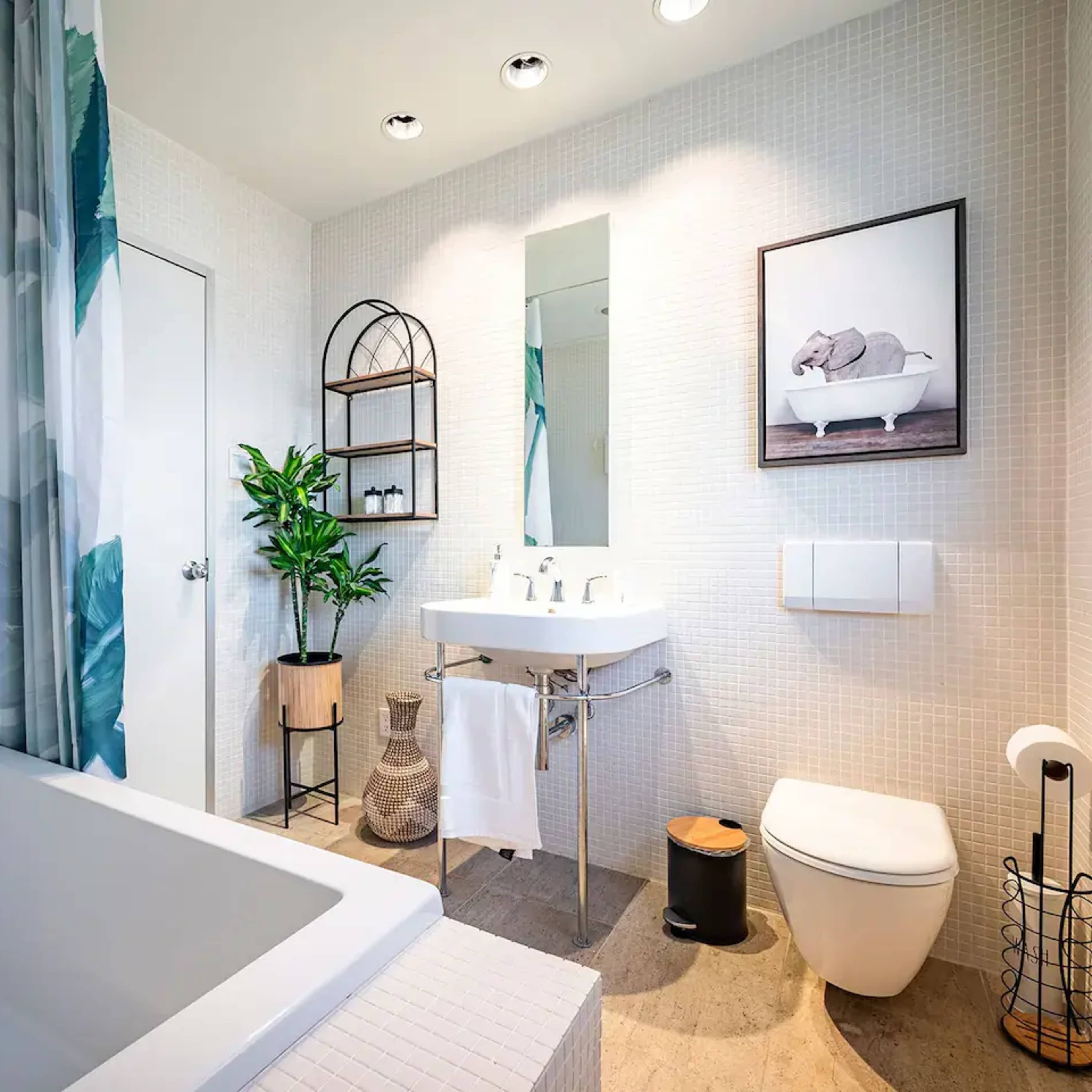 A modern bathroom features a bathtub, a sink with a mirror above, a towel rack, and potted plants against tiled walls.