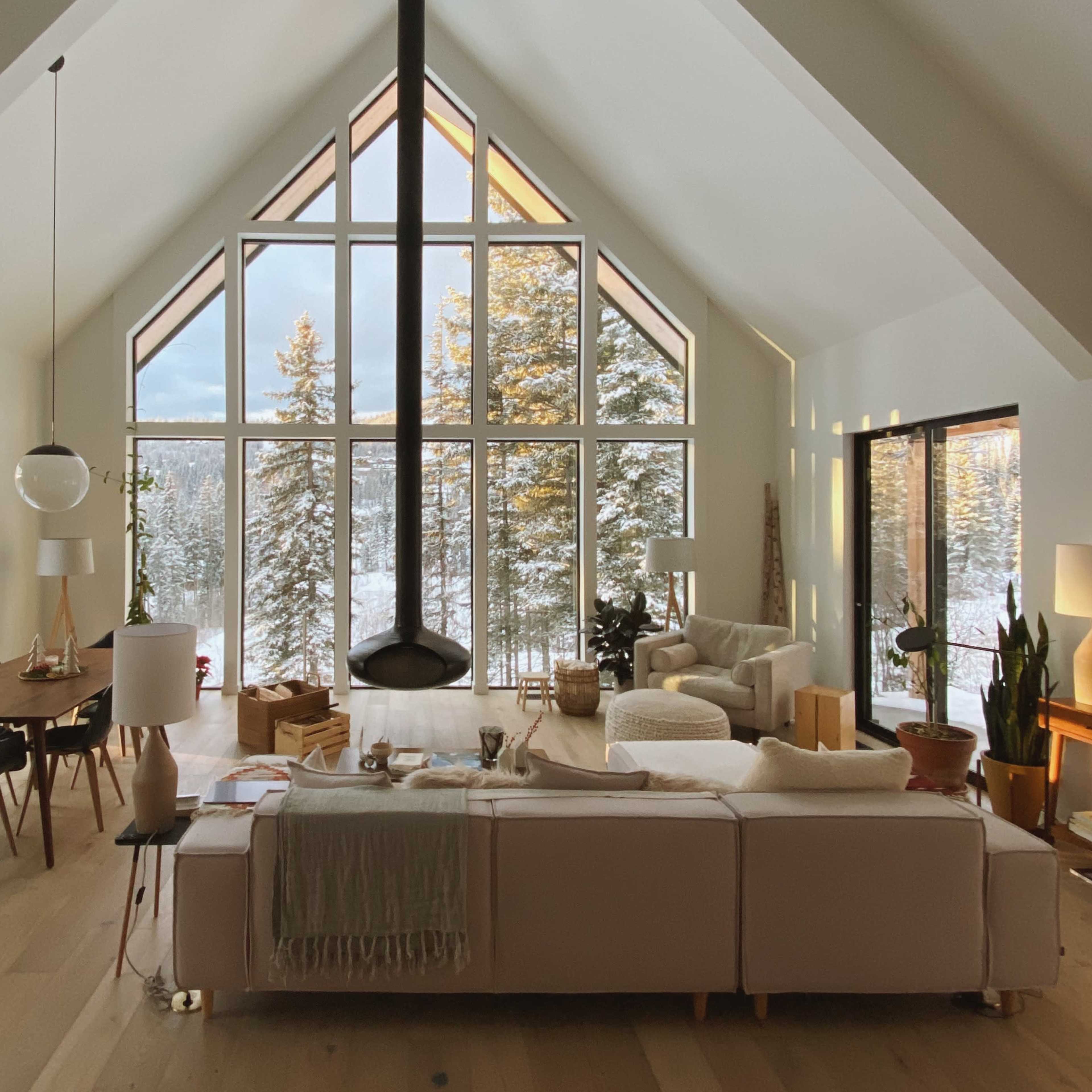 The living room features large windows overlooking a snowy forest, with modern furniture arranged around a central fireplace.