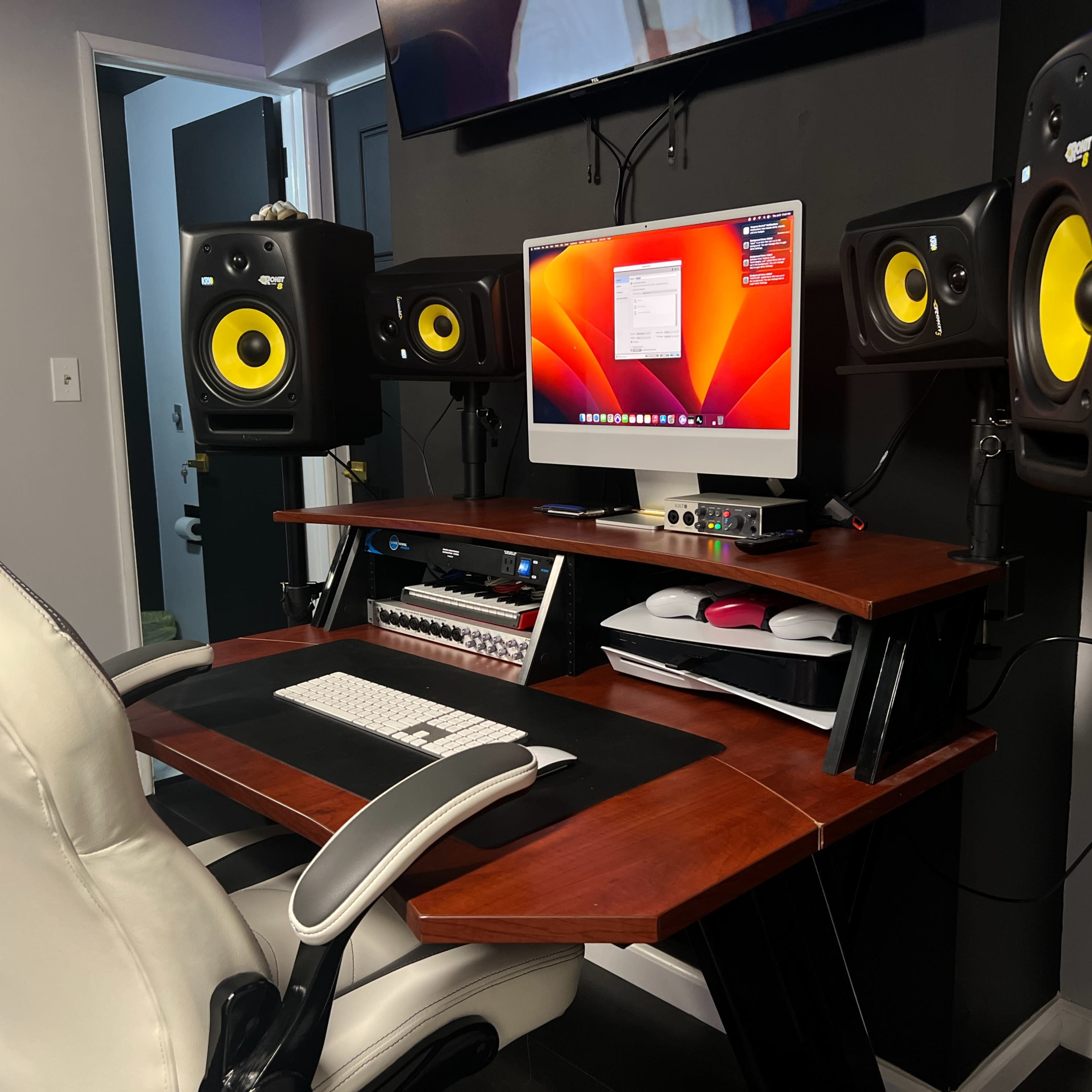 A workspace featuring a wooden desk with a computer monitor, audio speakers on either side, and a keyboard, all arranged in a modern studio setup.