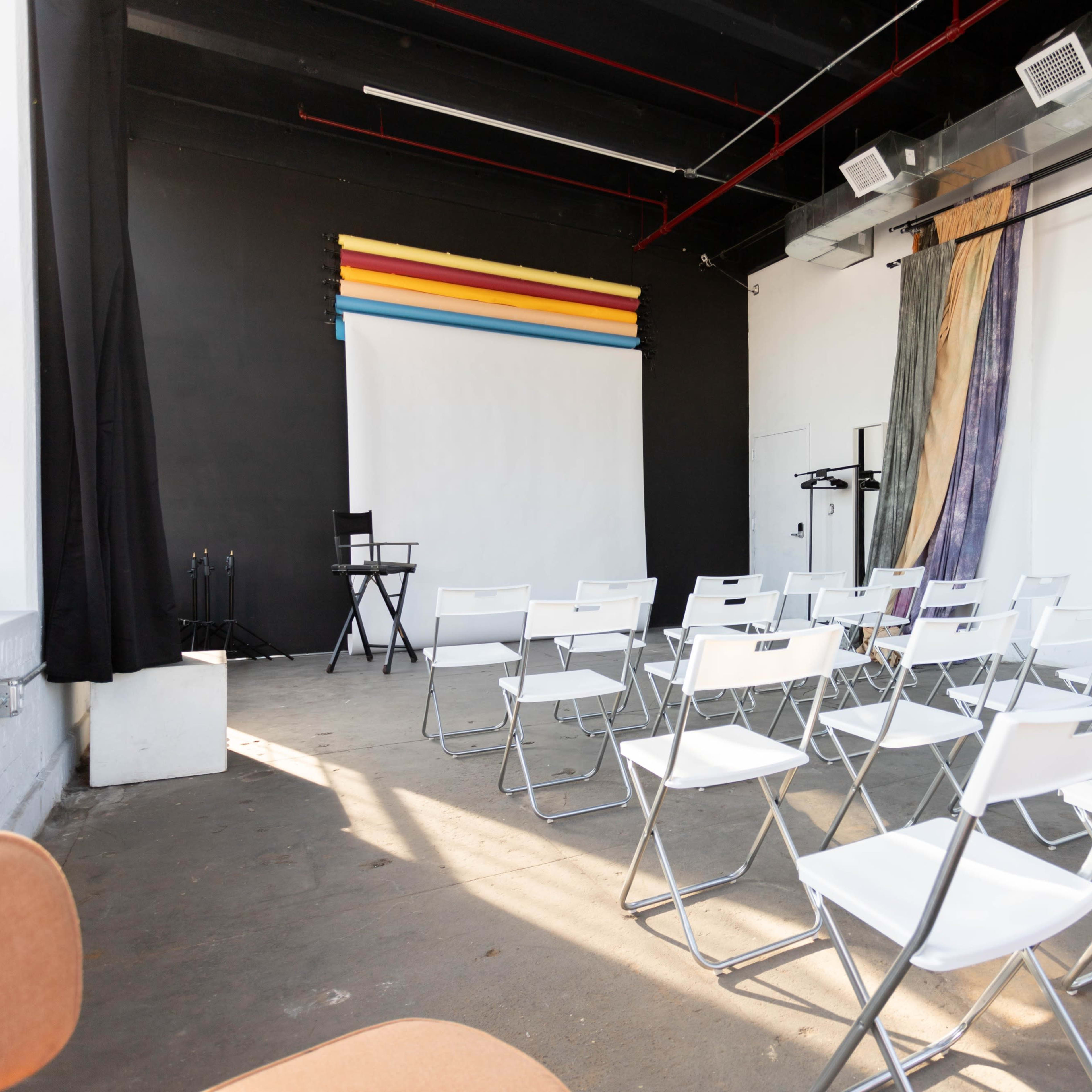 A spacious room with rows of white folding chairs facing a blank screen on a black wall.