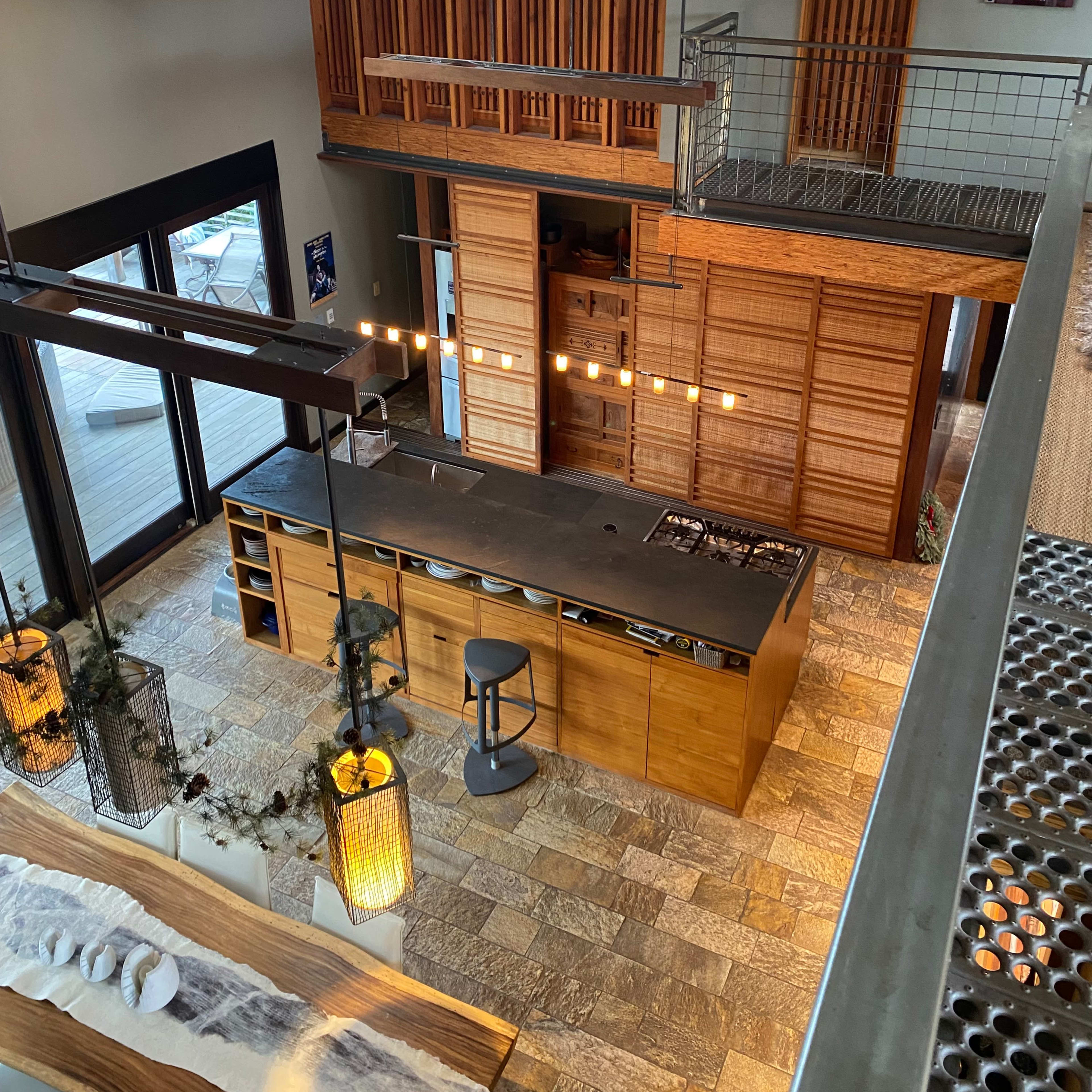 A modern kitchen space with wooden cabinetry, a large island, and a high ceiling, viewed from an upper level.
