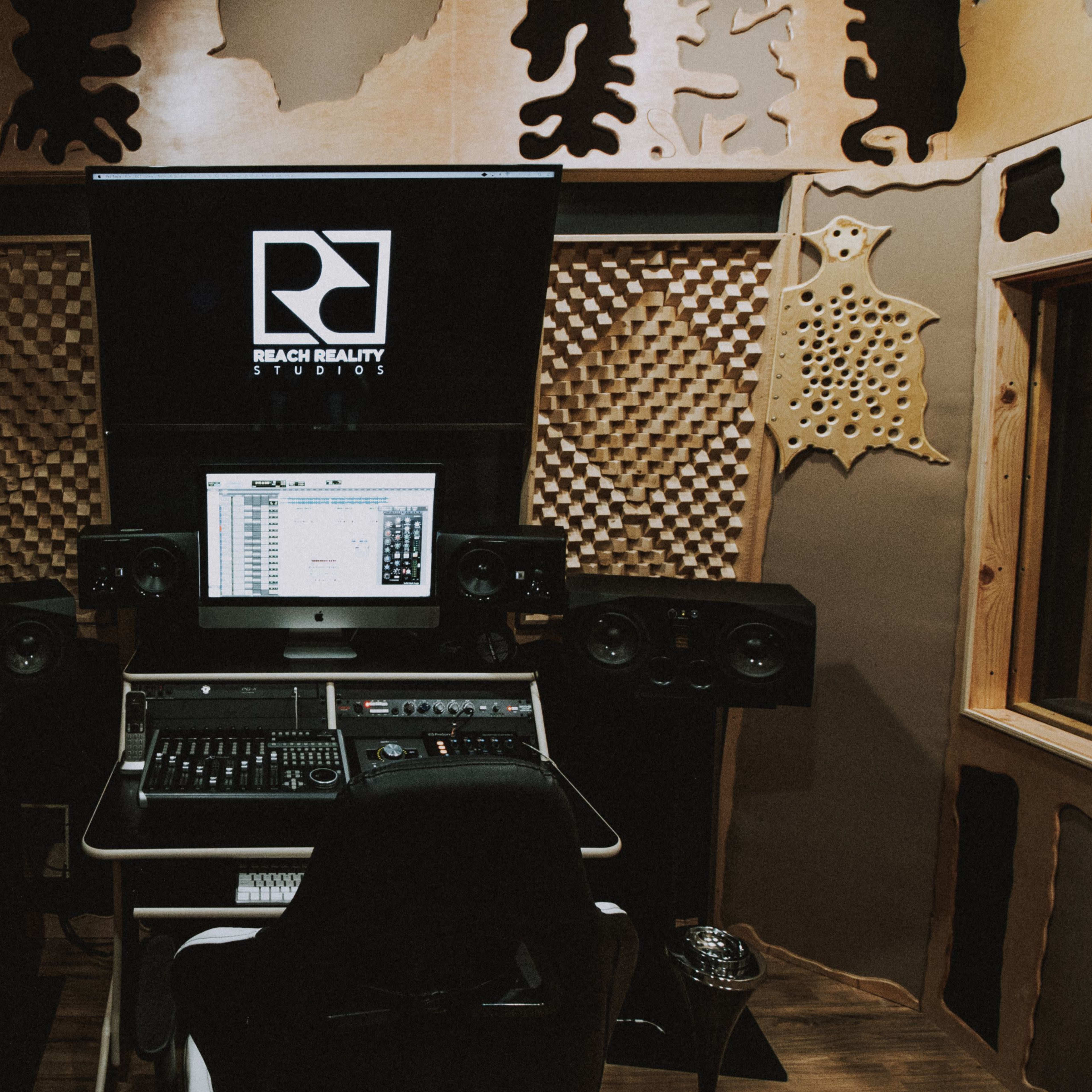 A music recording studio featuring a computer workstation with speakers, acoustic panels, and musical instruments.