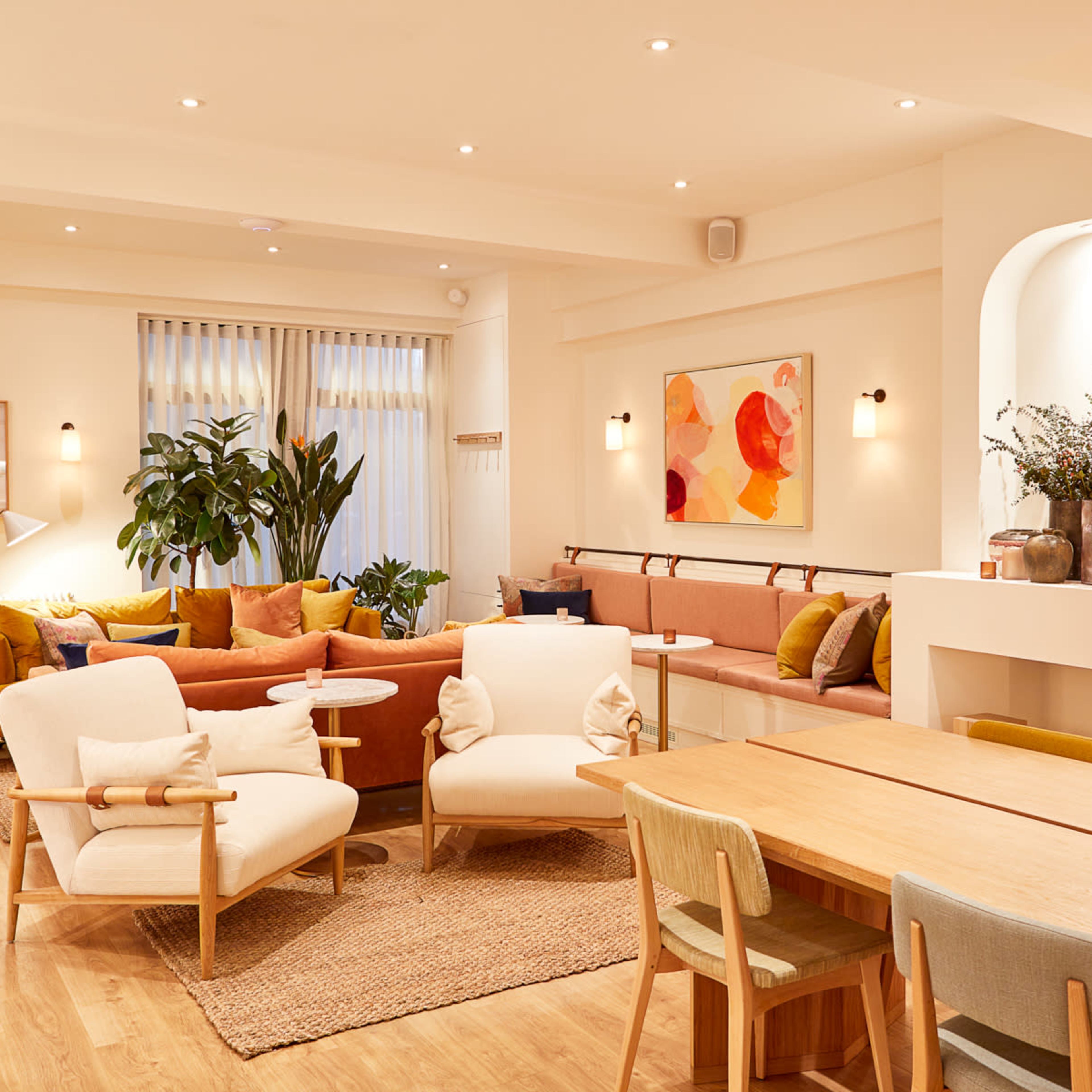 A bright and stylish lounge area with sofas, armchairs, and wooden tables, surrounded by indoor plants and decorative artwork.