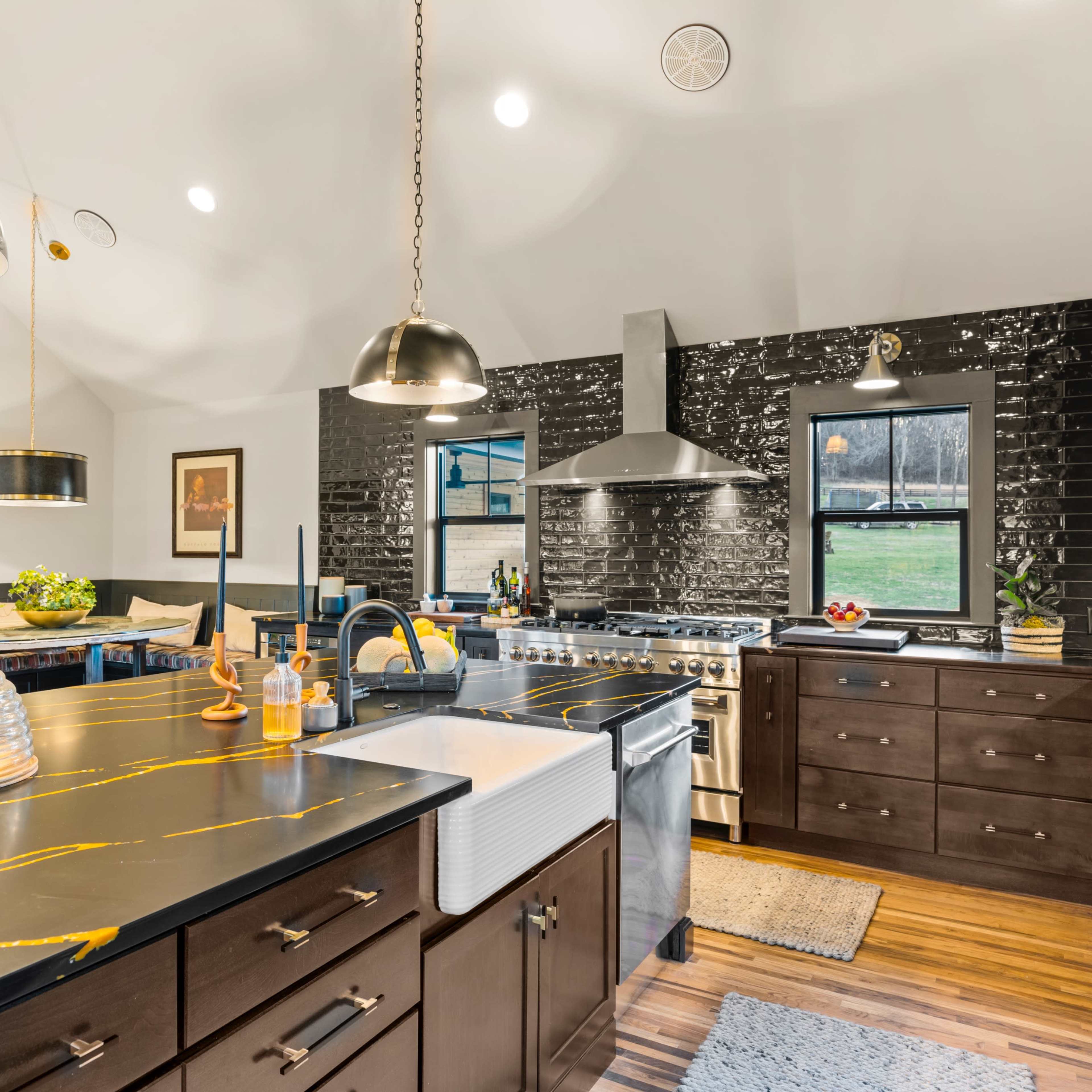The kitchen features a large island with a black countertop and gold veining, stainless steel appliances, and a mix of pendant lighting above.