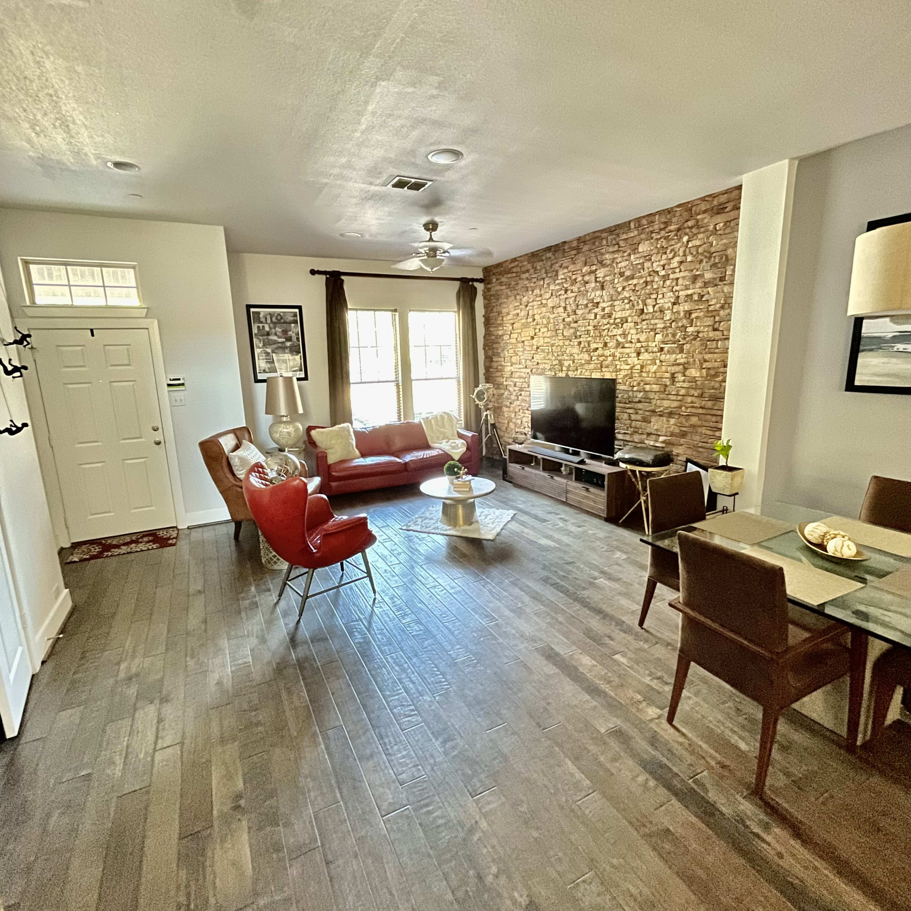 A living room with a stone accent wall, a television unit, a red sofa, and a dining area with wooden chairs.