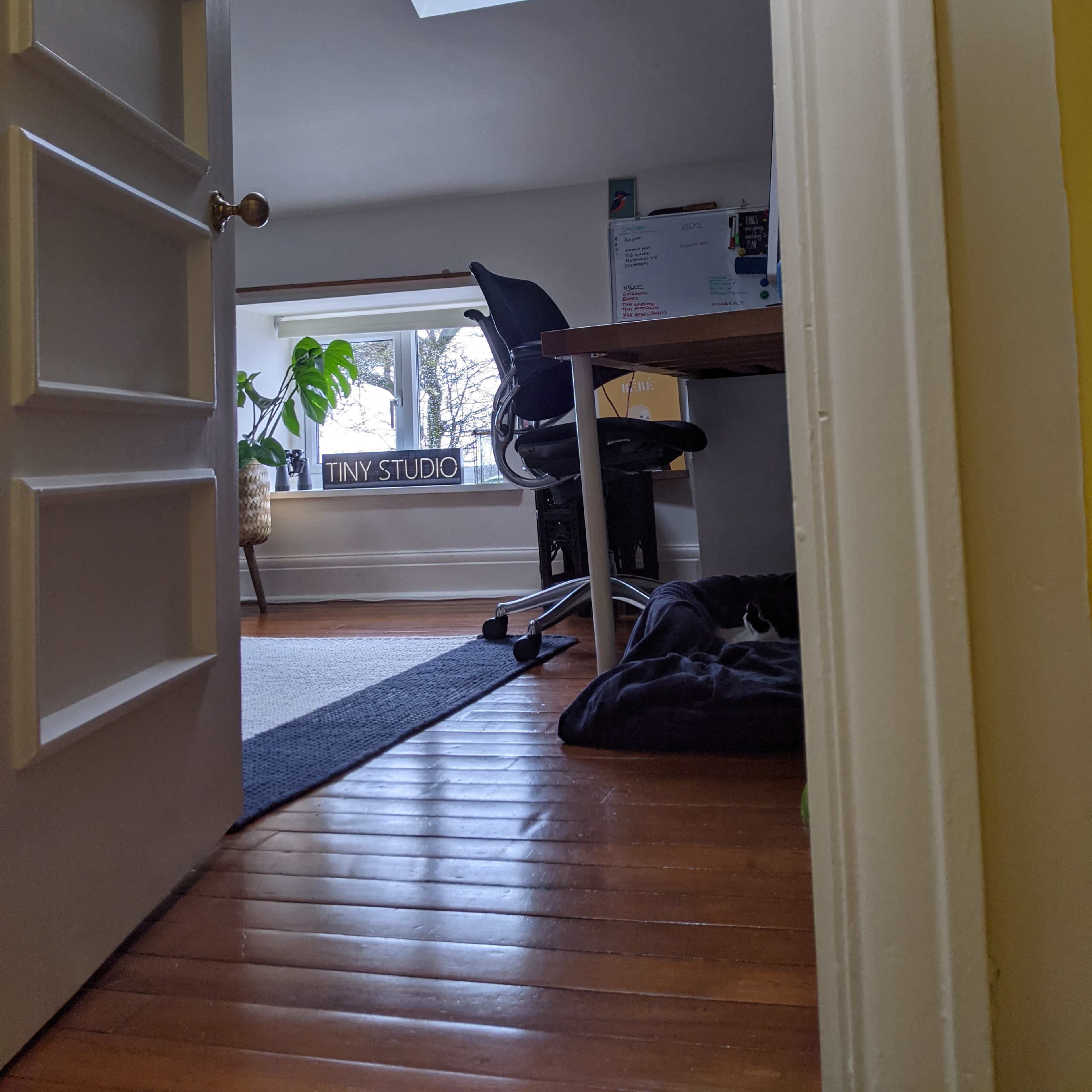 A partially open door reveals a small studio with a desk and chair under a skylight.