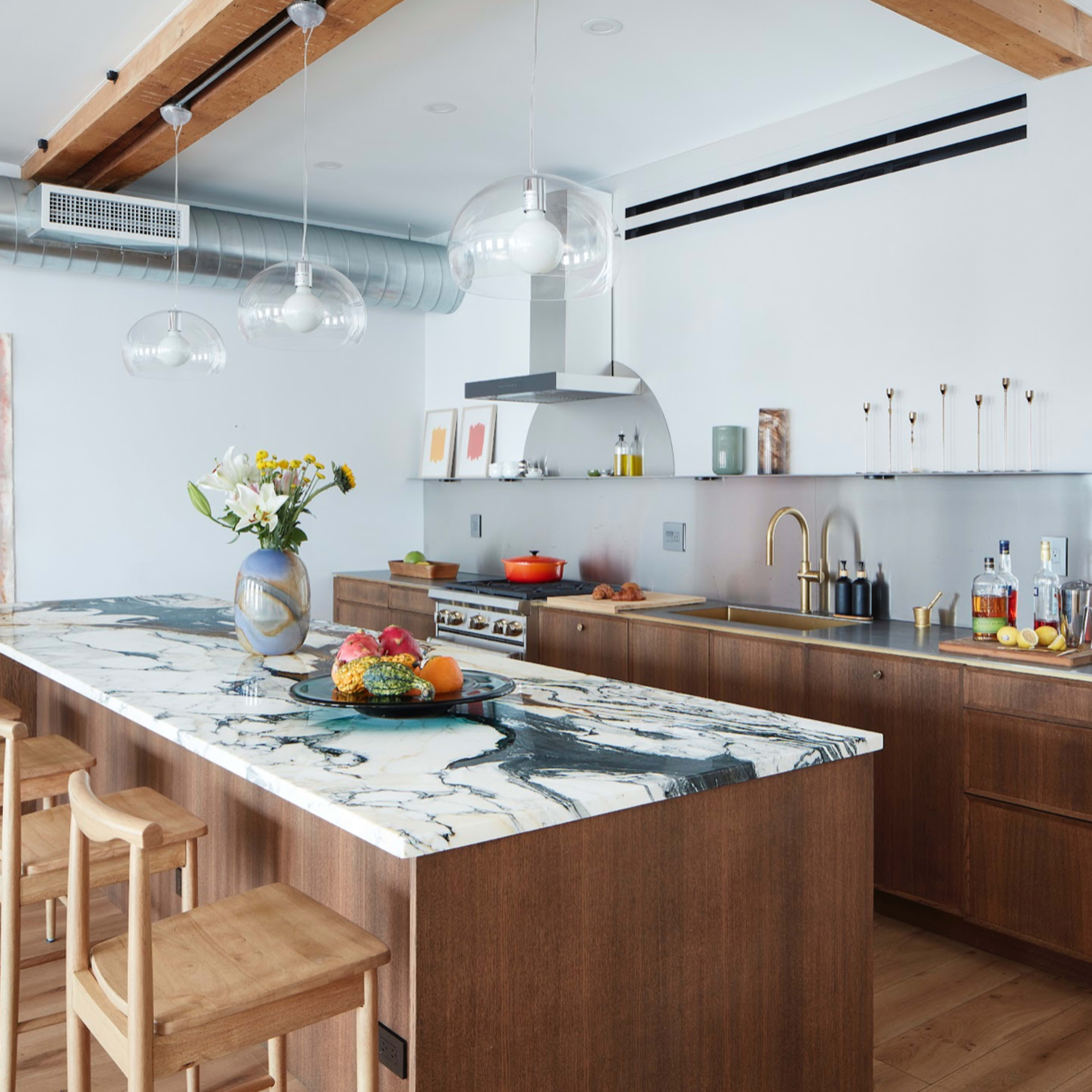 A modern kitchen features a wooden island with a marble countertop, stainless steel appliances, and light wood bar stools.