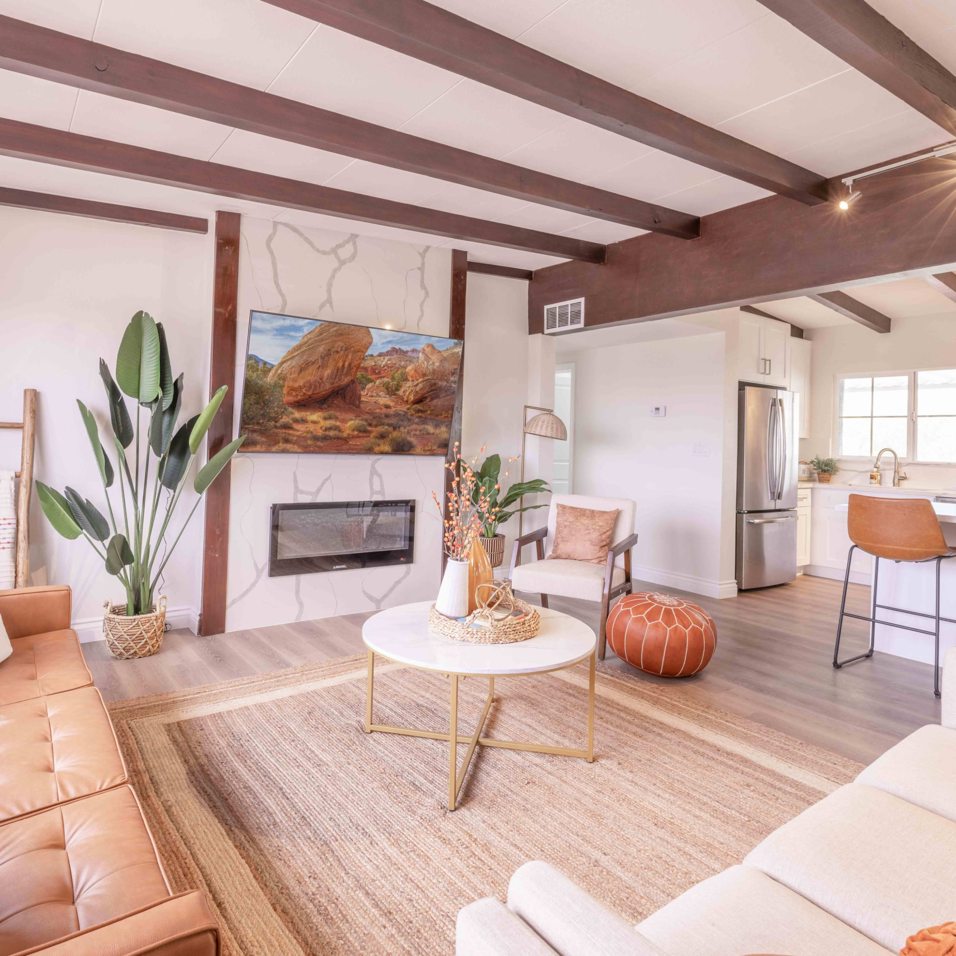 A modern living room with a tan leather sofa, a circular coffee table, and an artwork featuring a rock landscape hanging above a minimalistic fireplace.