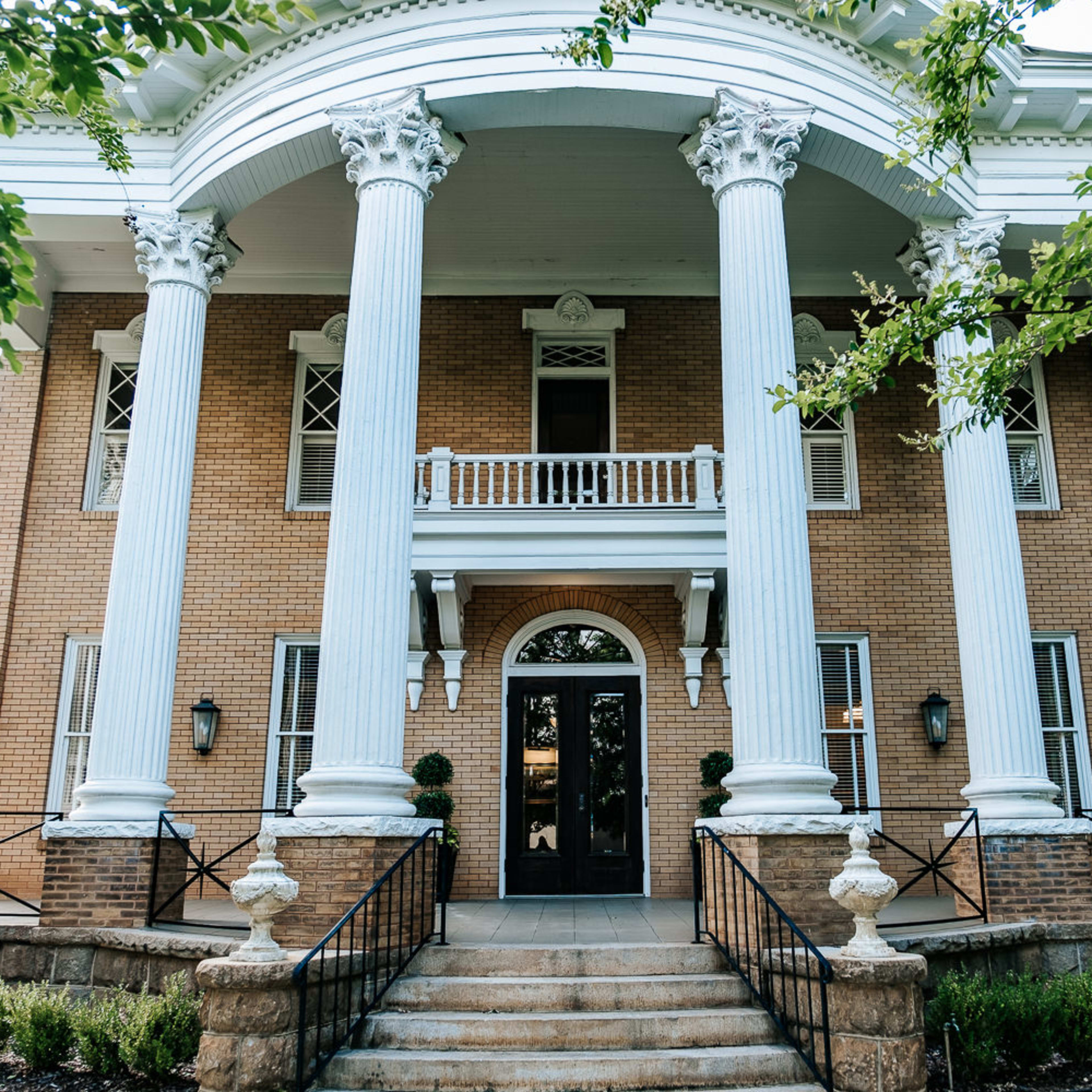 A two-story brick mansion with a grand entrance featuring tall white columns and a wide staircase.