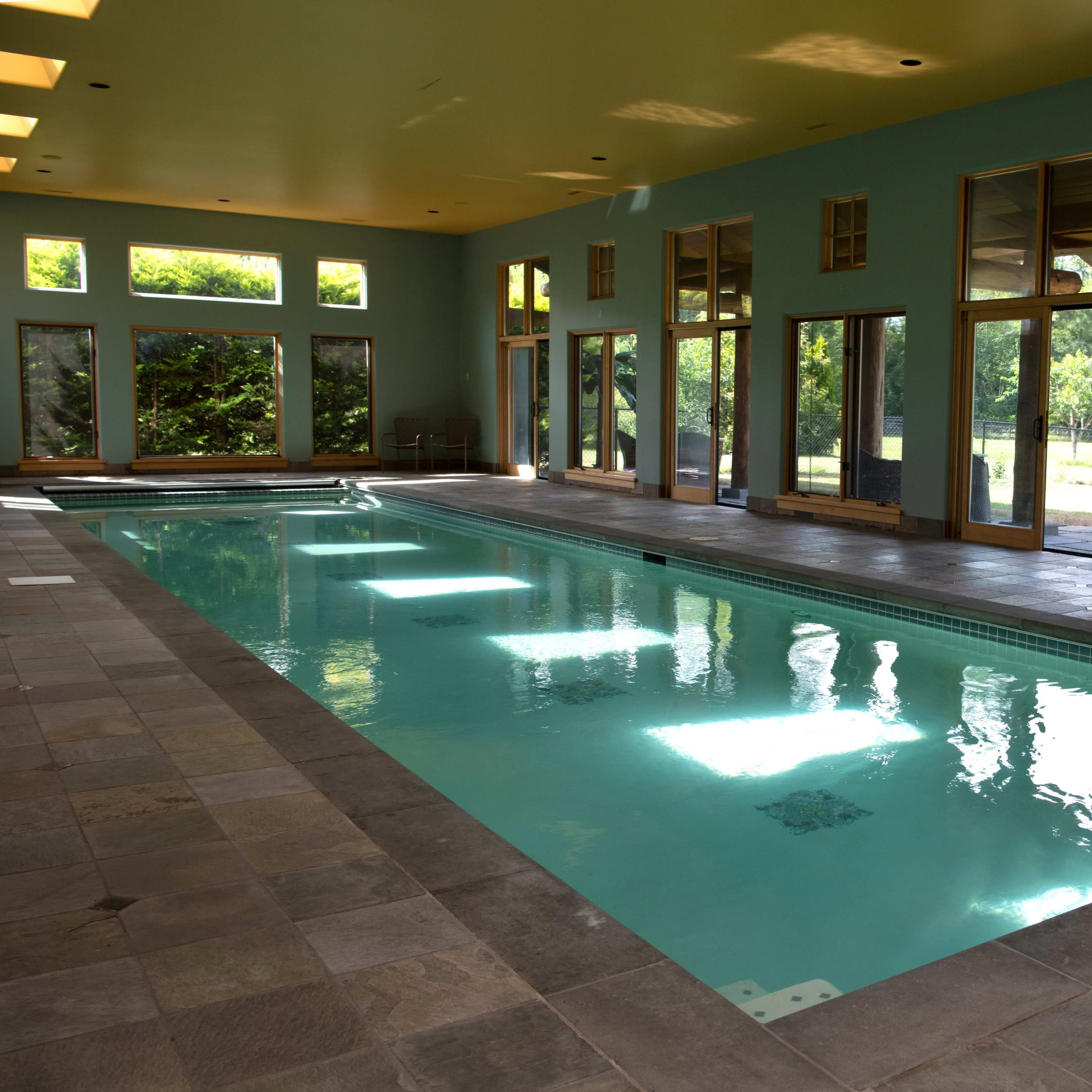 An indoor swimming pool with large windows that overlook a green outdoor area.
