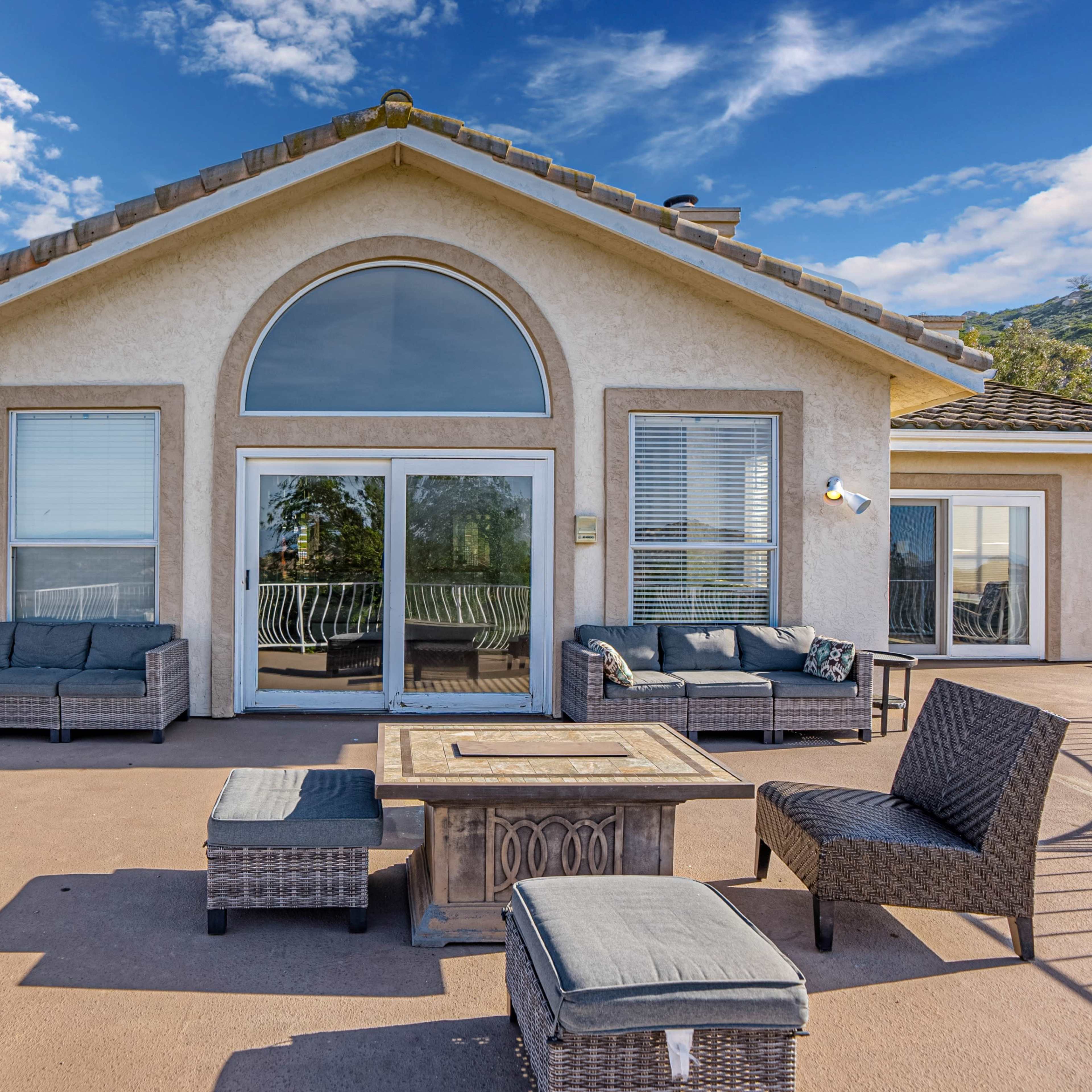 A large, modern house features a spacious deck with outdoor seating and scenic views of the surrounding landscape.