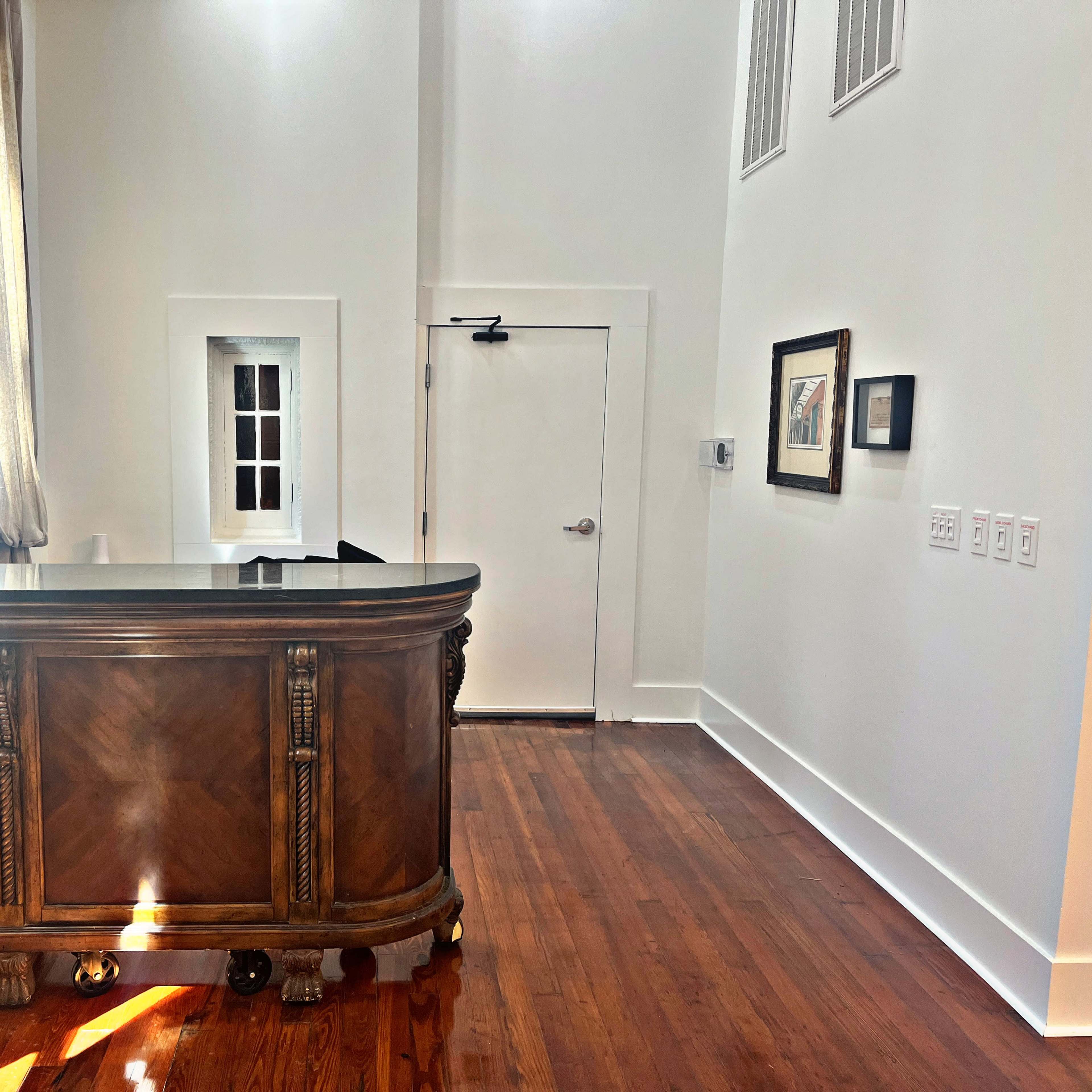 A wooden reception desk positioned against a white wall in a brightly lit room with hardwood flooring.