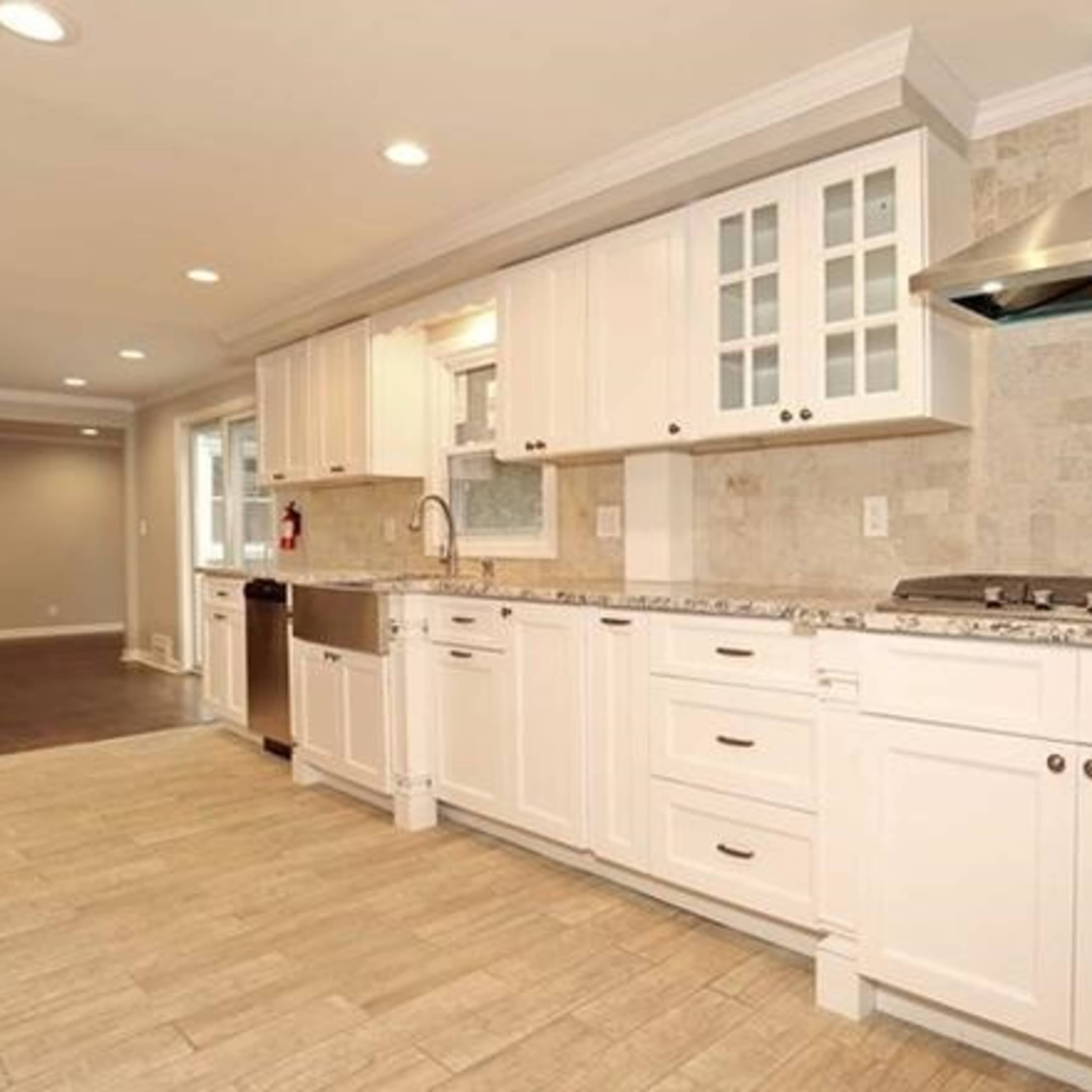 A modern kitchen with white cabinets, a stainless steel range hood, and a tiled backsplash, featuring a countertop with a double sink and a combination of built-in and under-counter appliances.