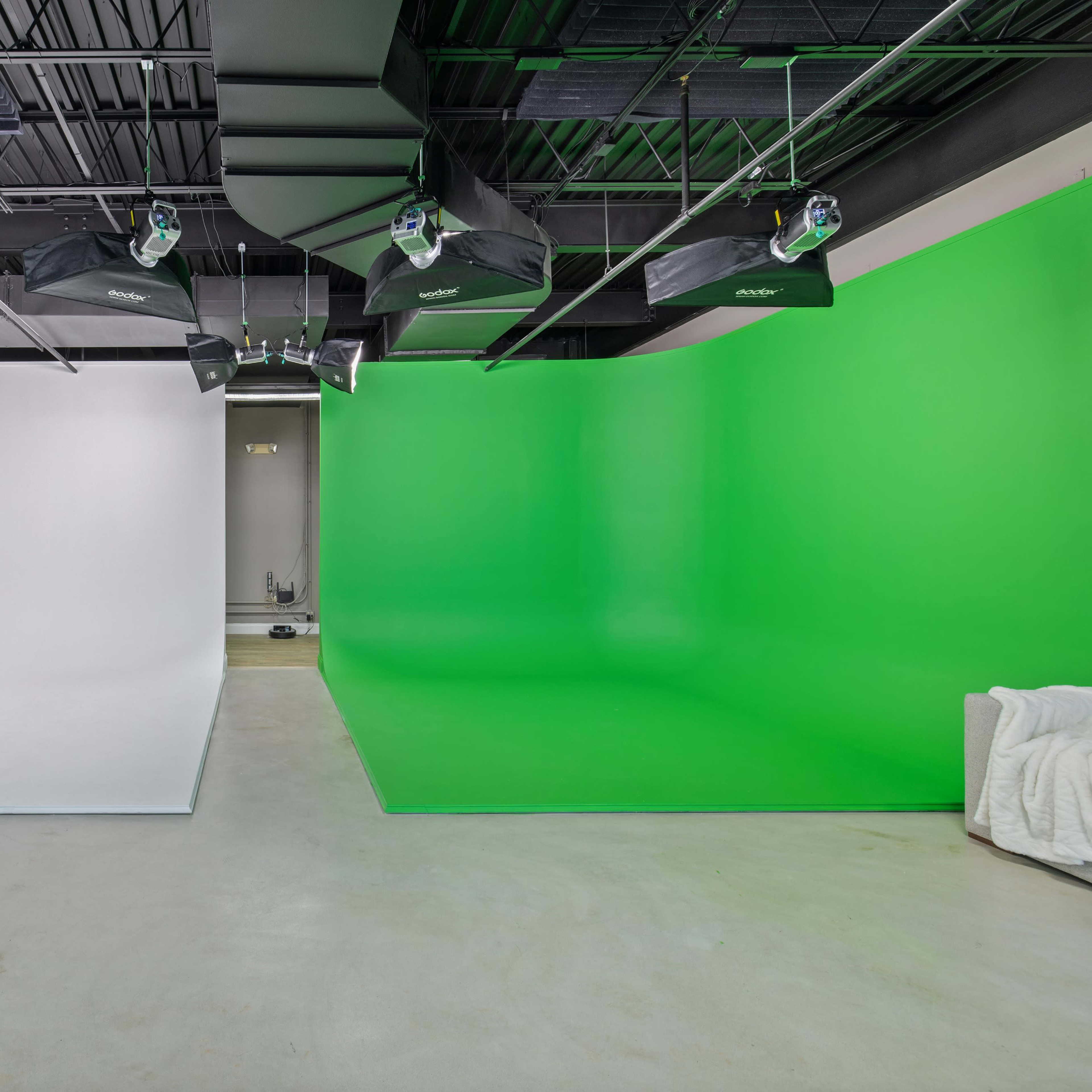 A photography studio with a large white backdrop on one side and a green screen backdrop on the other.