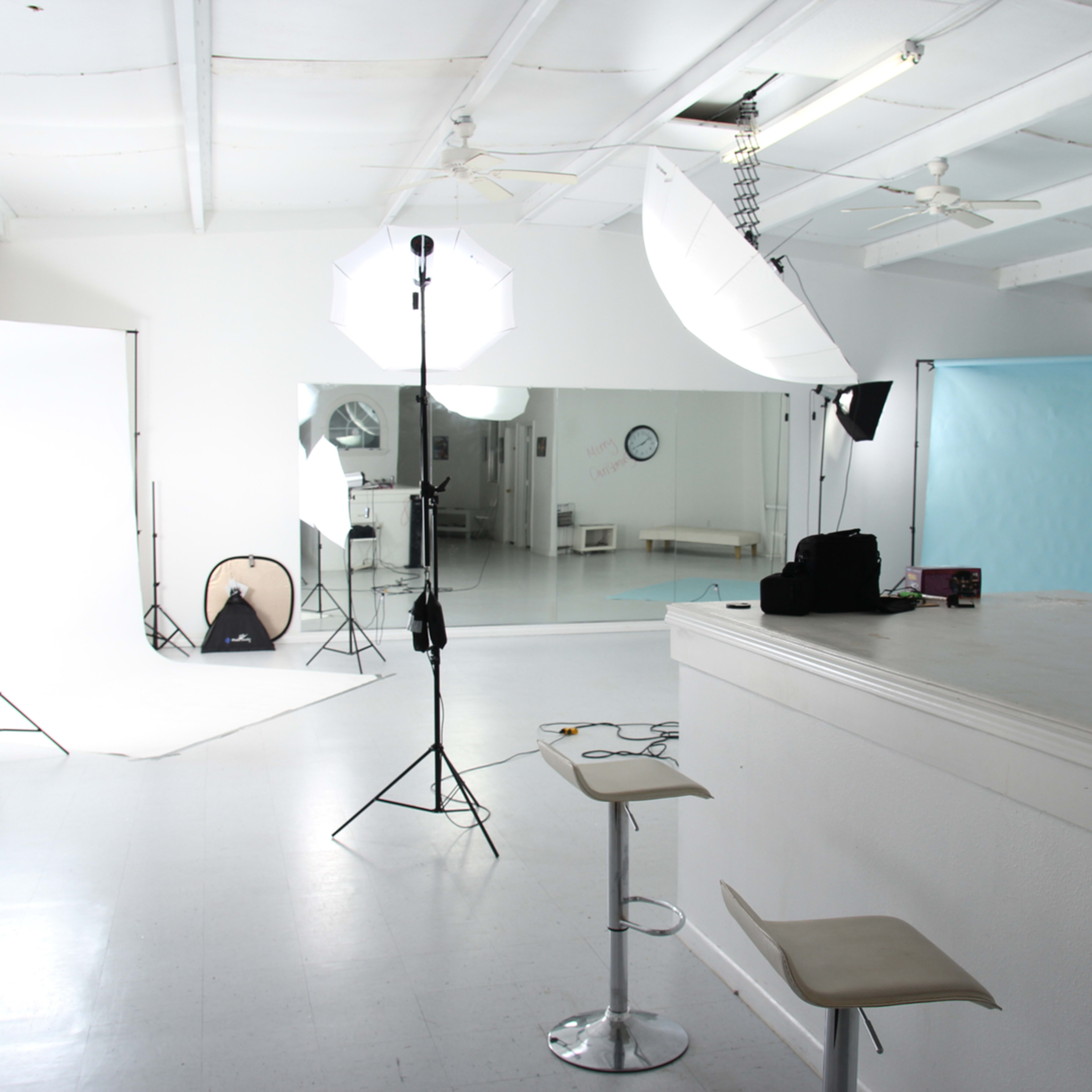 A photography studio features lighting equipment, backdrop stands, and a bar area with stools.