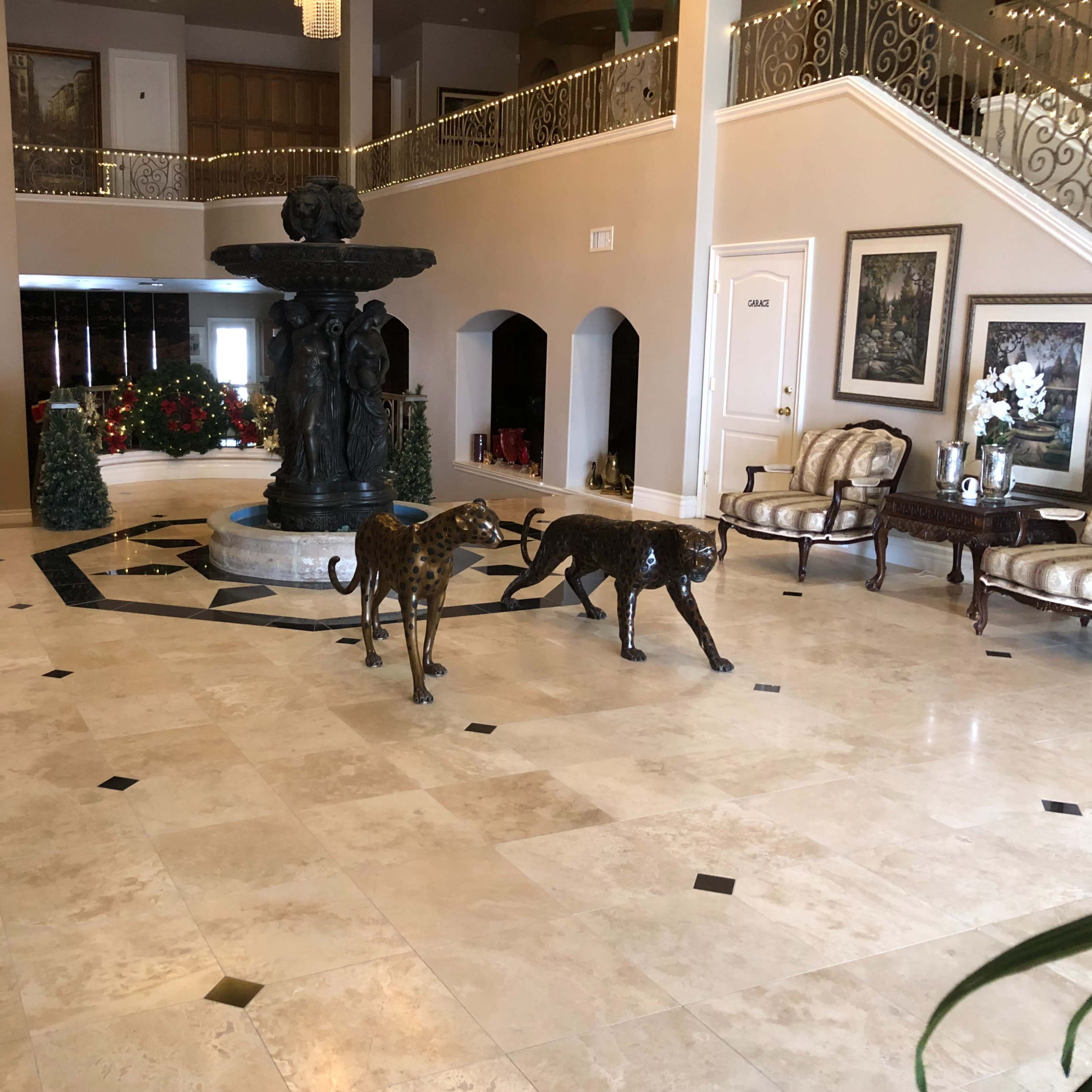 A spacious foyer with a marble floor, featuring a central fountain and two bronze leopard sculptures on display.