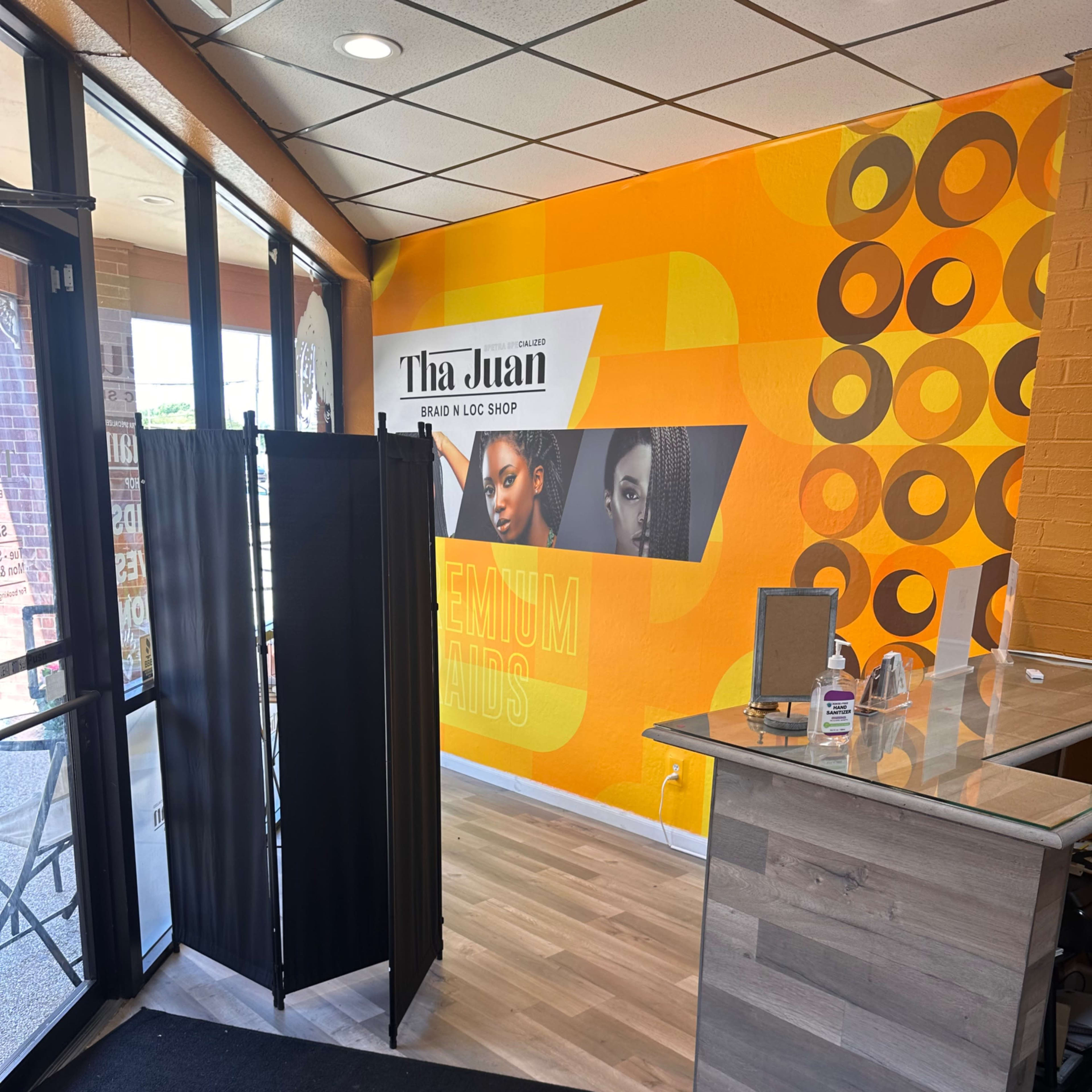 The interior of a salon features a reception area with a black privacy screen and an orange accent wall displaying promotional graphics.