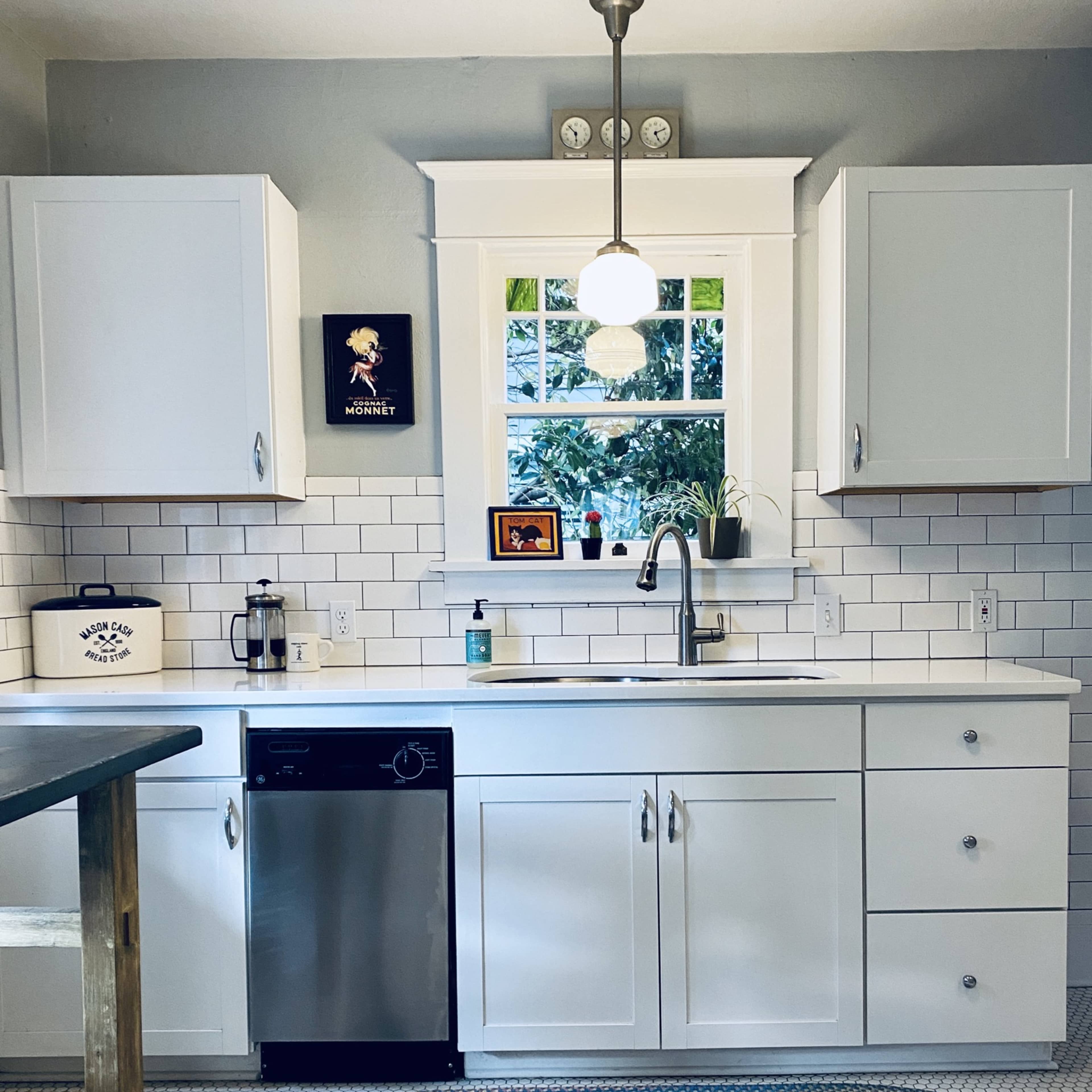 A modern kitchen features white cabinets, a stainless steel dishwasher, and a window with a view, complemented by a colorful woven rug on the tiled floor.