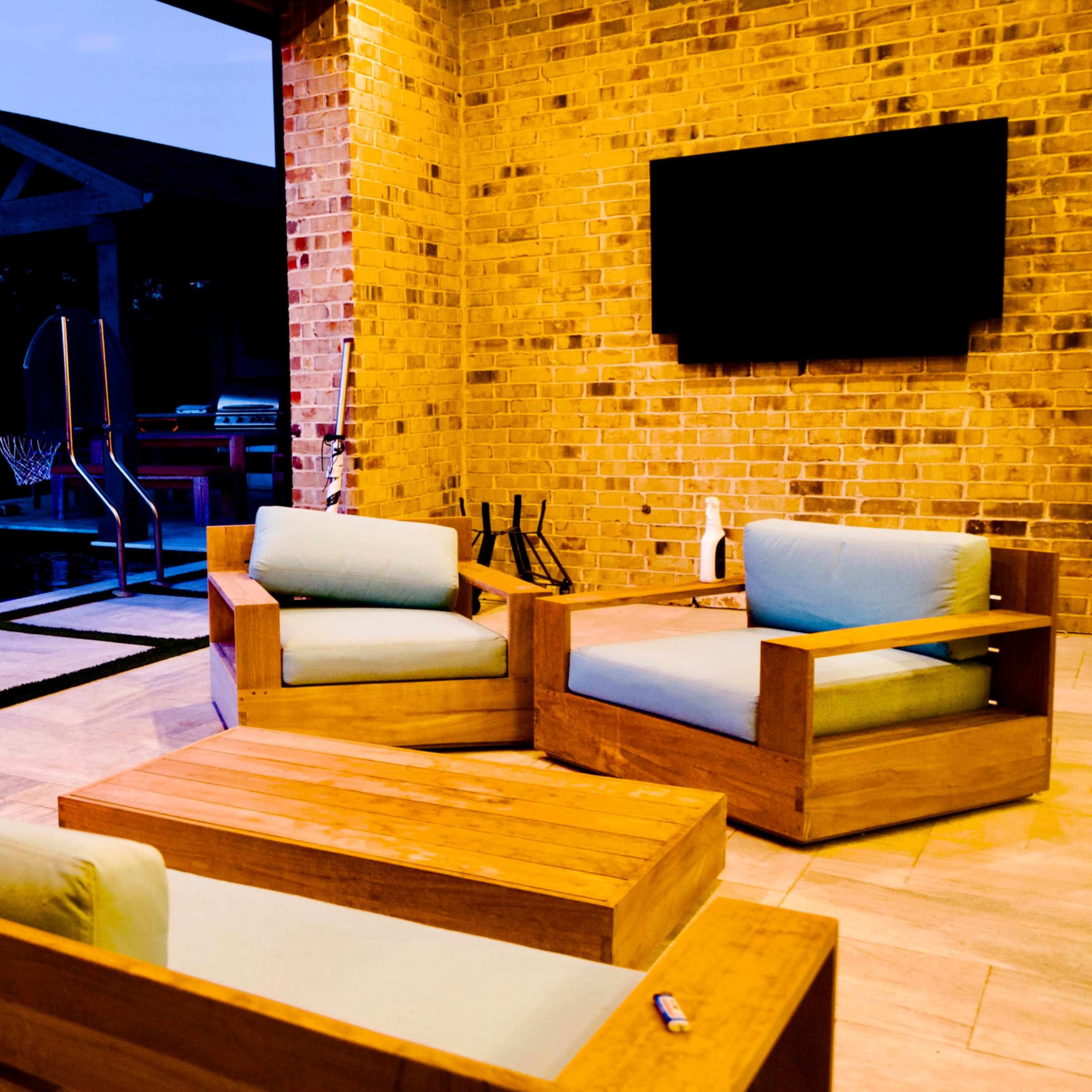 An outdoor seating area features wooden furniture and a pool, illuminated during twilight.