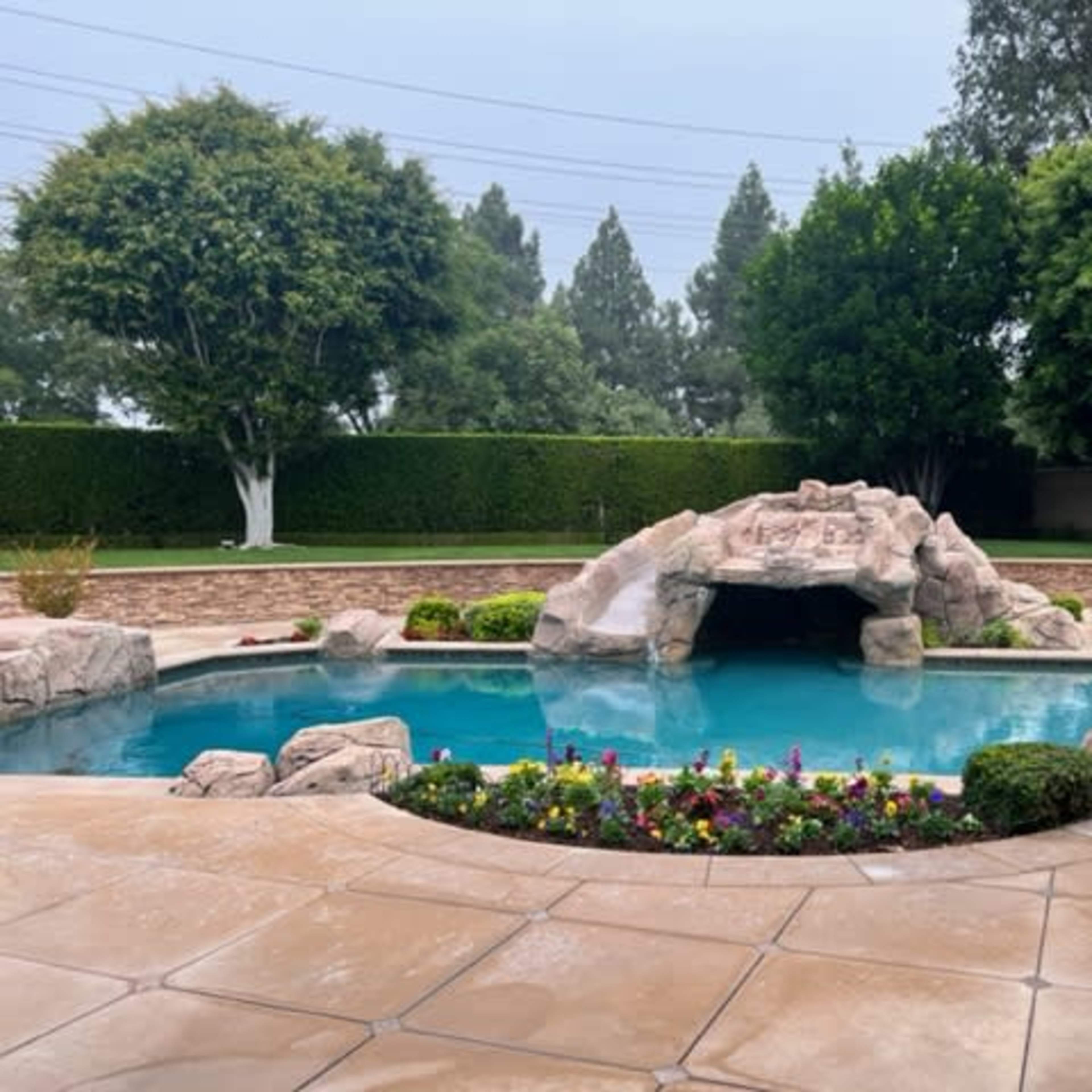 A landscaped backyard with a swimming pool featuring a rock formation and colorful flower beds.