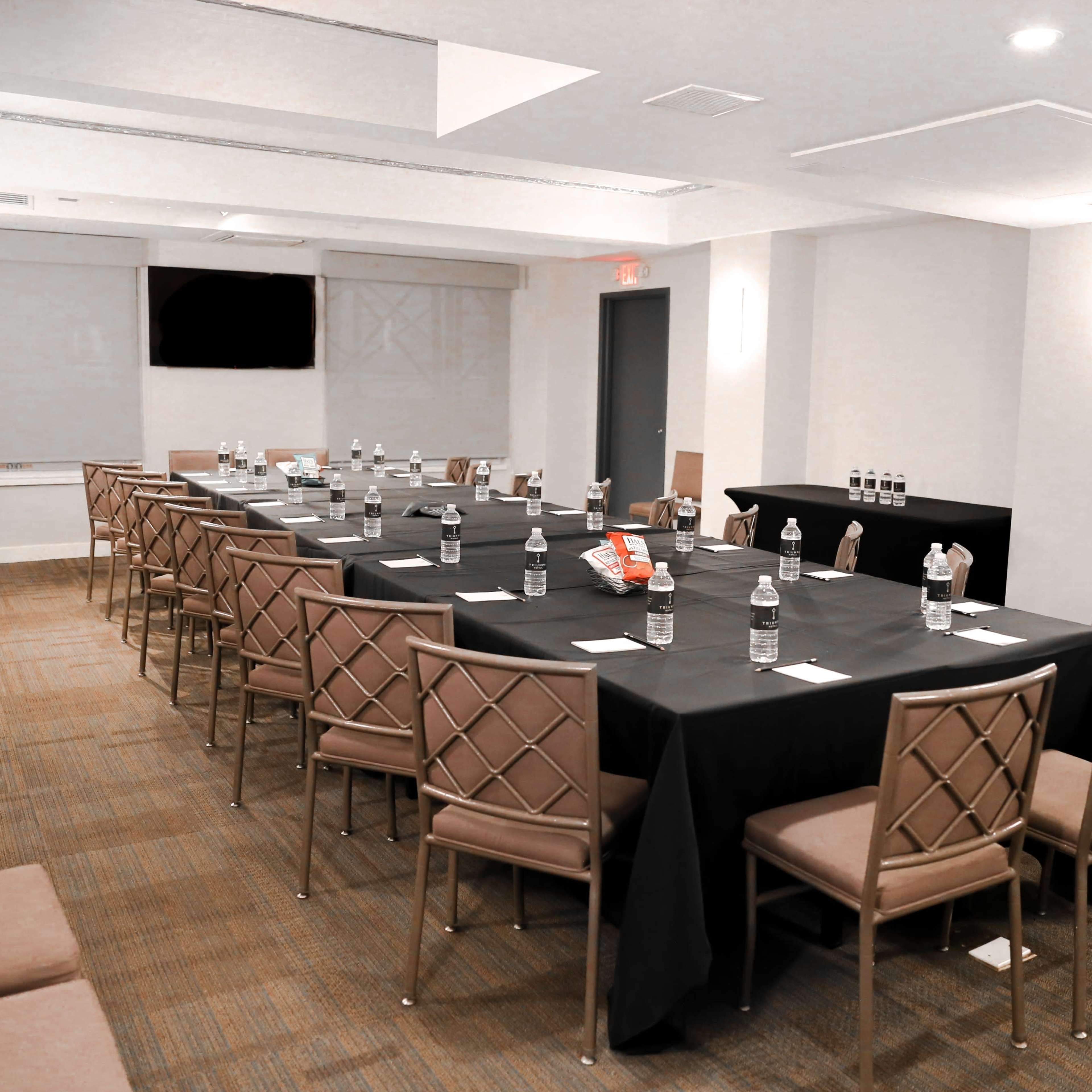 A long conference table is set with water bottles and snacks in a well-lit meeting room.