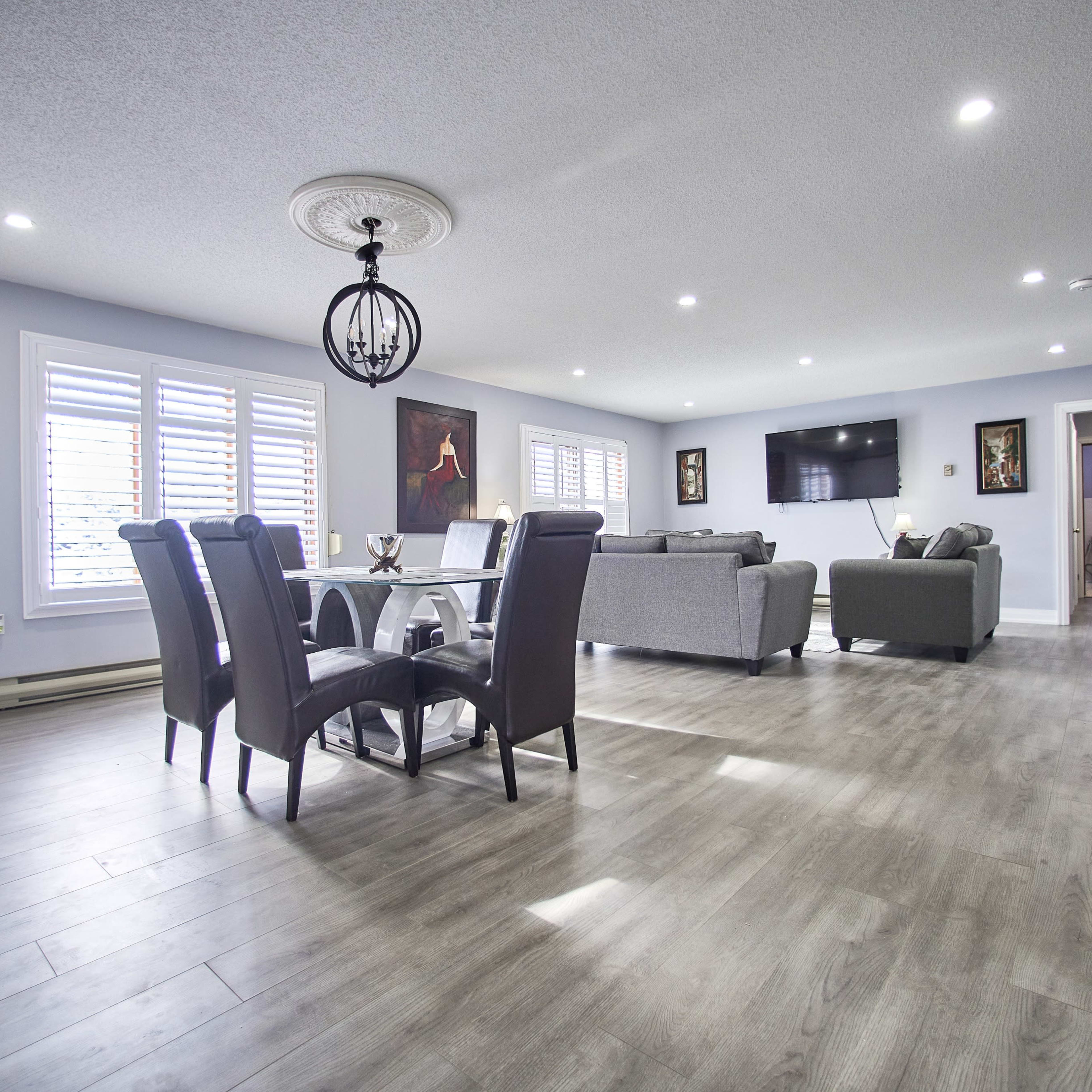 A well-lit living space with a dining area featuring a table and six chairs, a couch set, and a wall-mounted television.