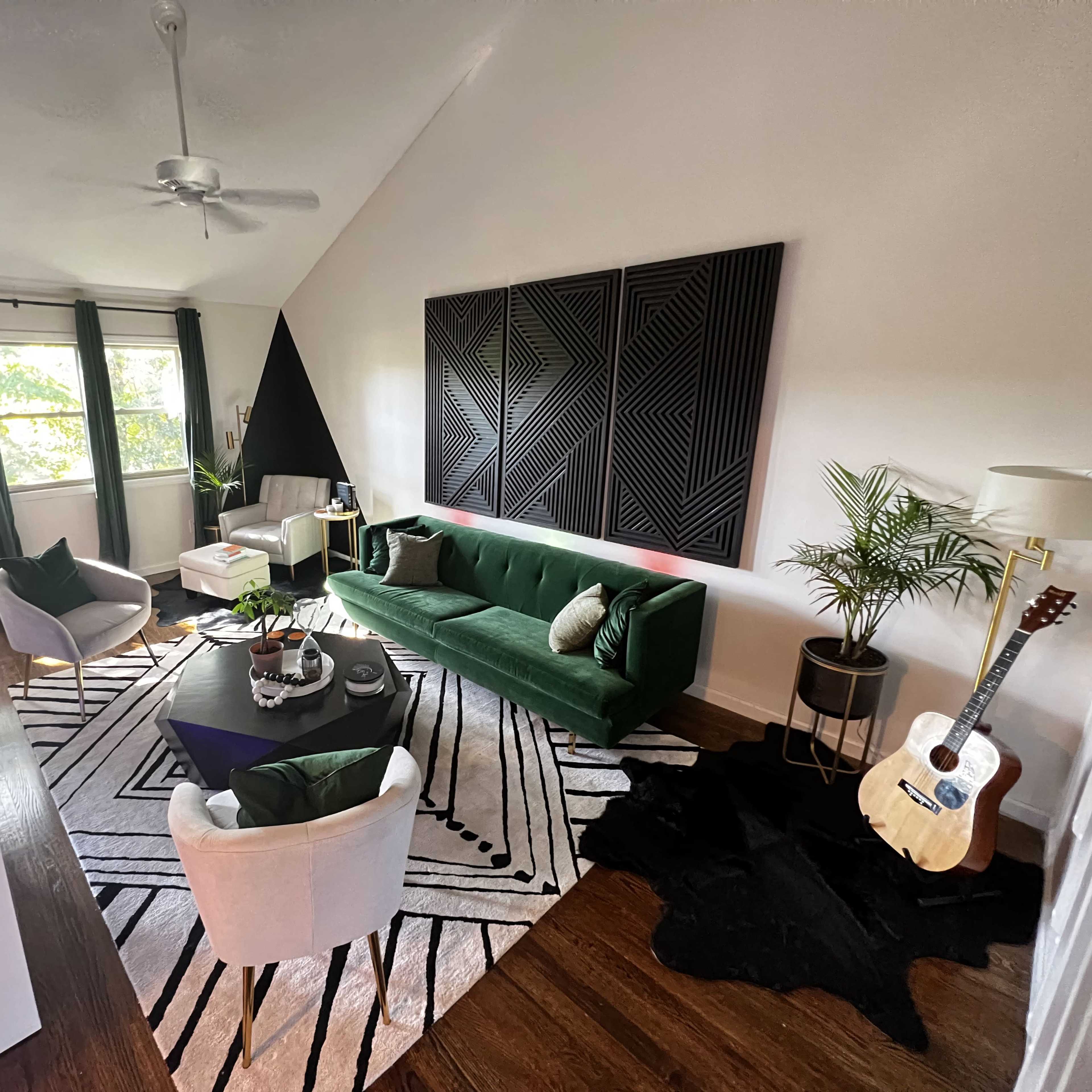 A modern living room featuring a green sofa, a round coffee table, a patterned rug, and large windows allowing natural light to fill the space.