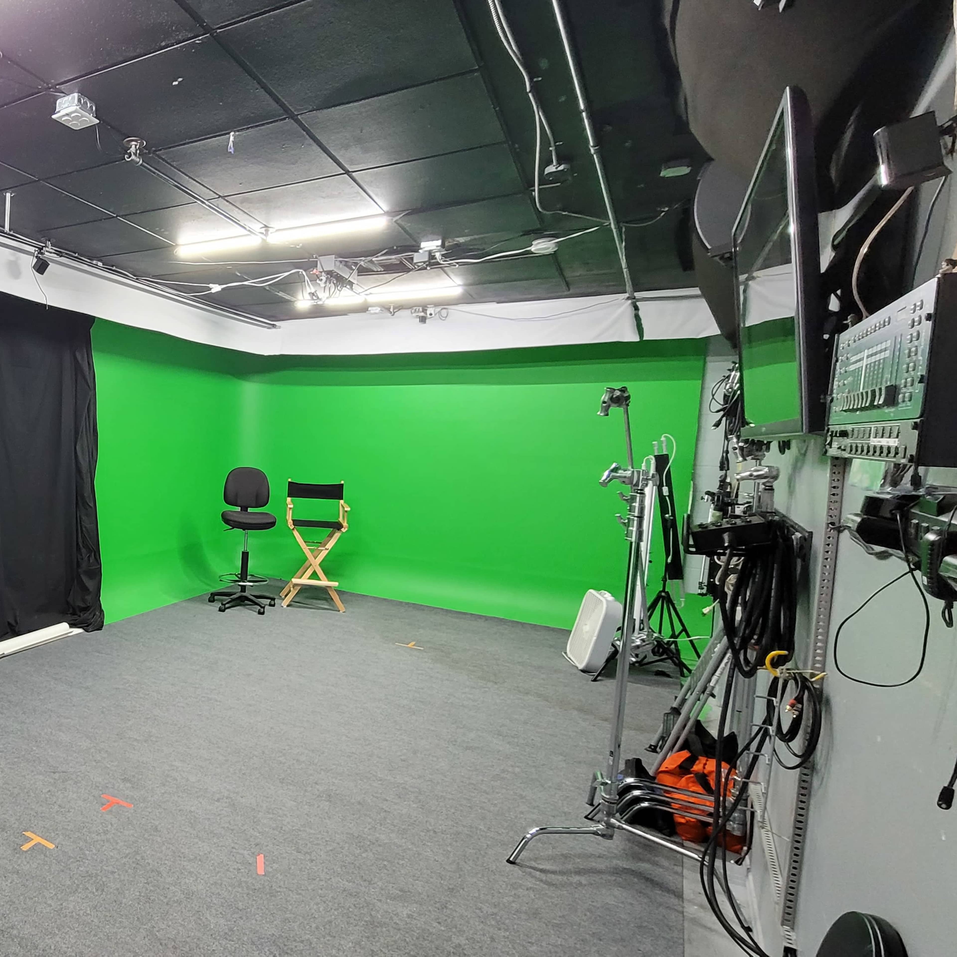 A green screen studio equipped with lighting, a chair, and various production equipment.