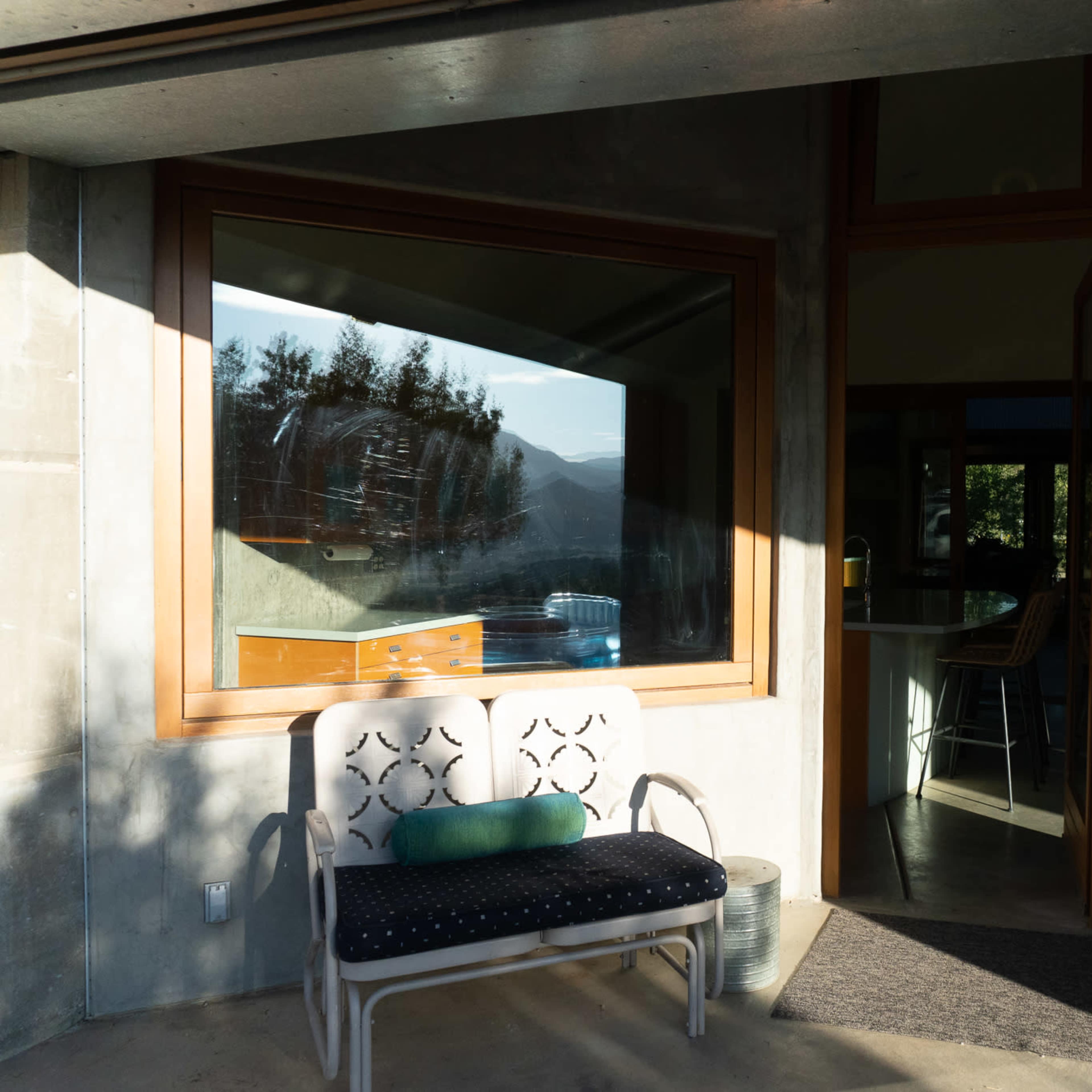 A bench sits in front of a modern glass window and wooden door, featuring a view of trees and mountains.