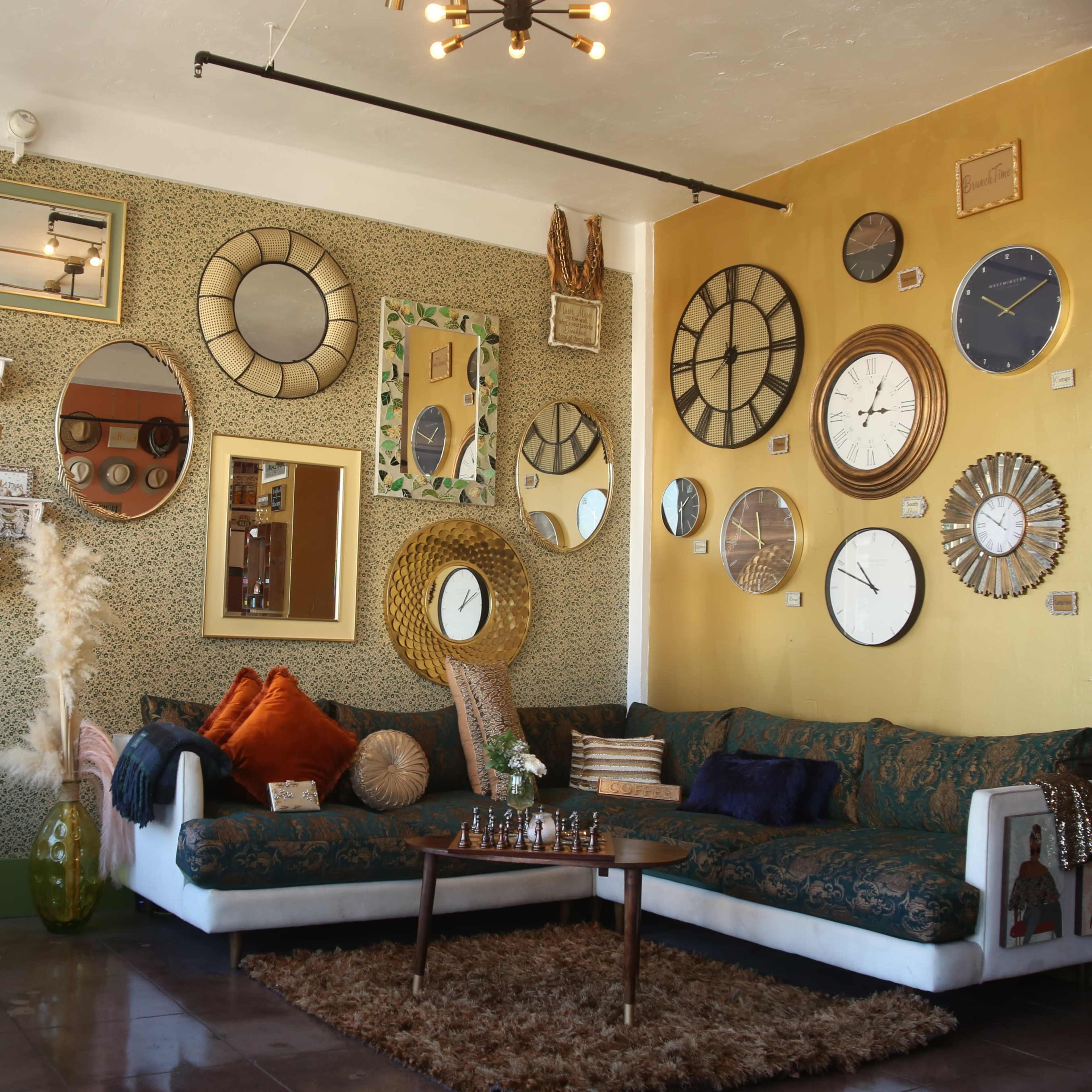 A cozy living room featuring a patterned wall adorned with various clocks and mirrors, a large sectional couch, and decorative plants.