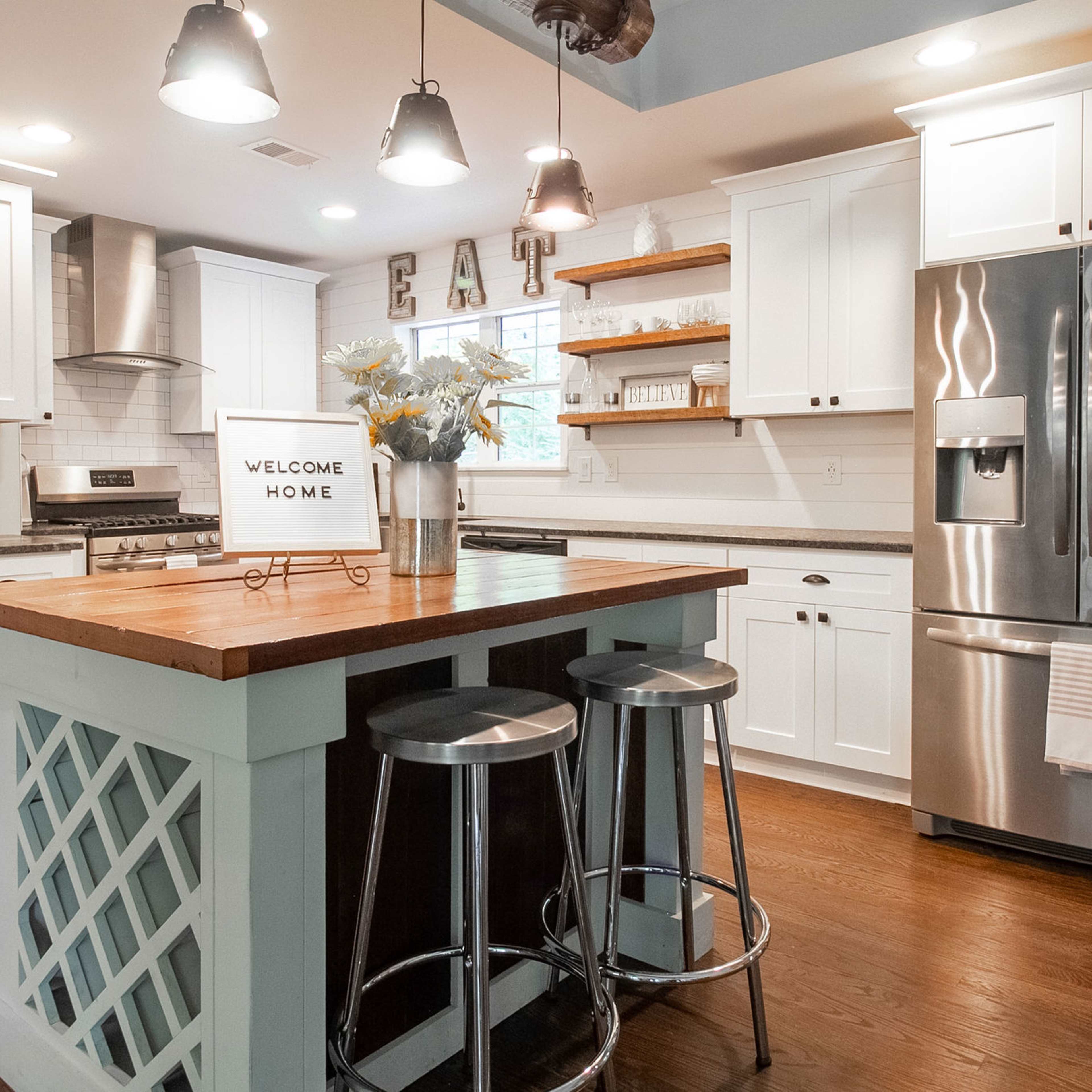A modern kitchen with white cabinetry, a wooden island, stainless steel appliances, and bar stools.