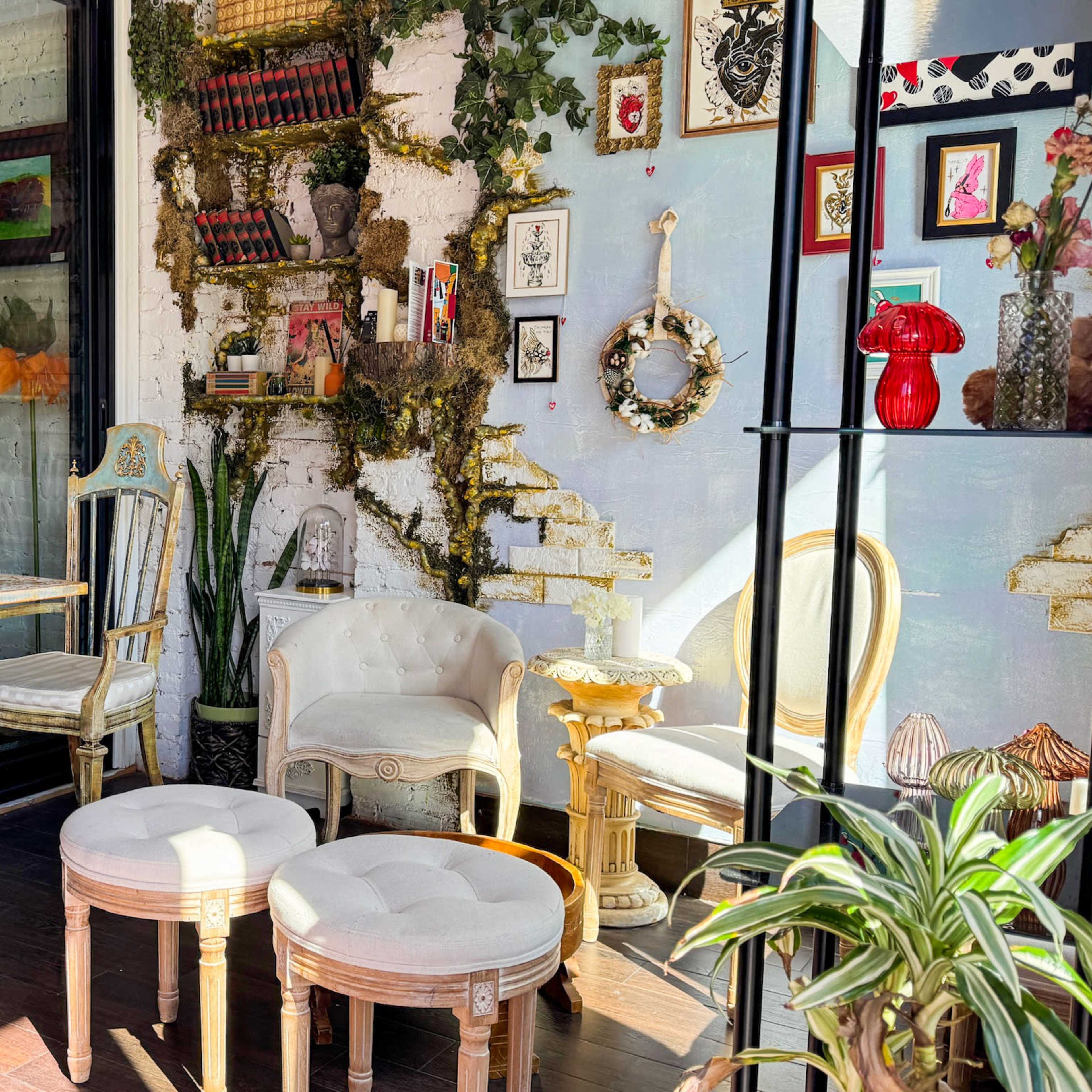 A cozy café interior with vintage seating, framed artwork on the walls, and decorative plants.