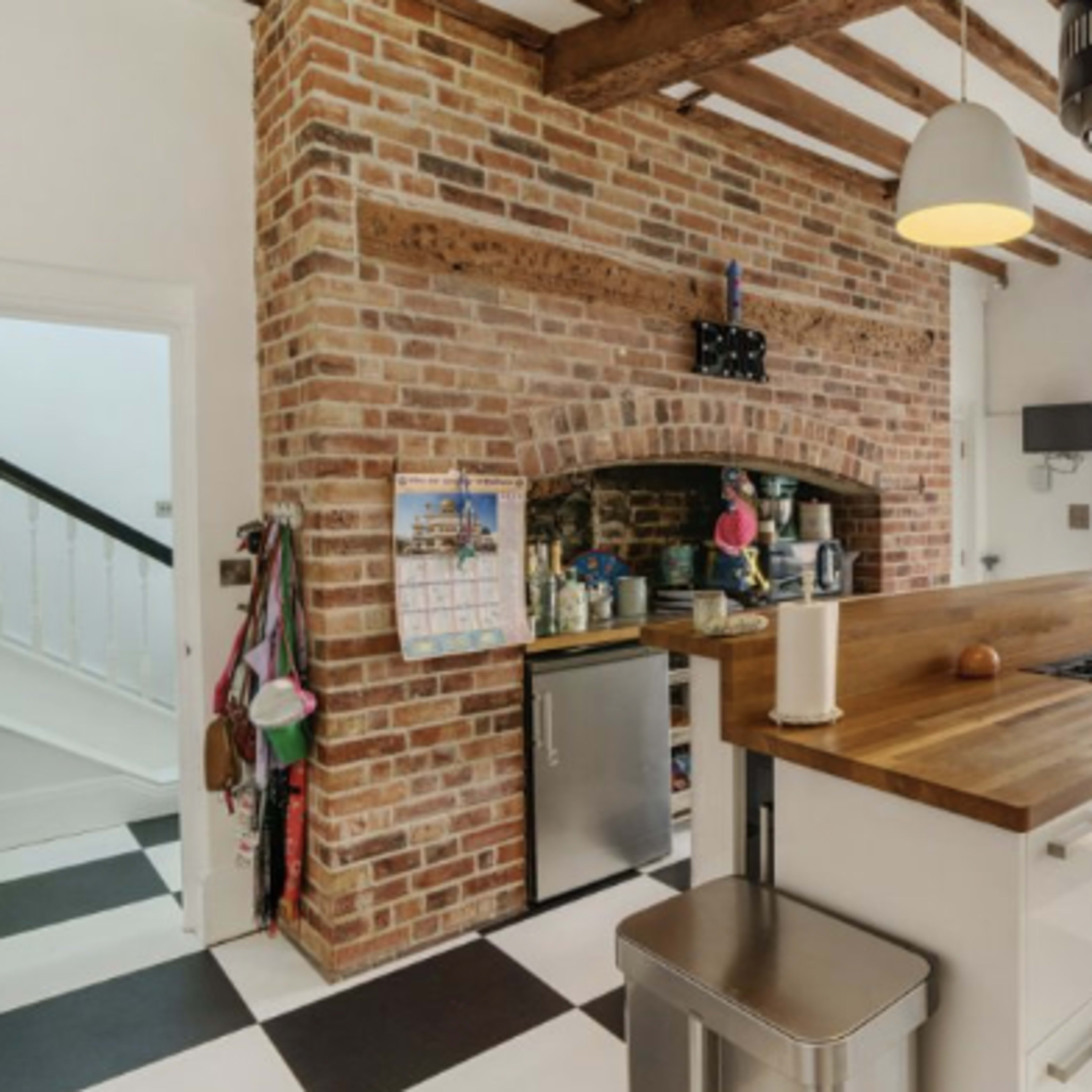 A modern kitchen featuring a brick accent wall, a large wooden island with a stove, and a checkerboard floor, with natural light flooding in from a nearby glass door.
