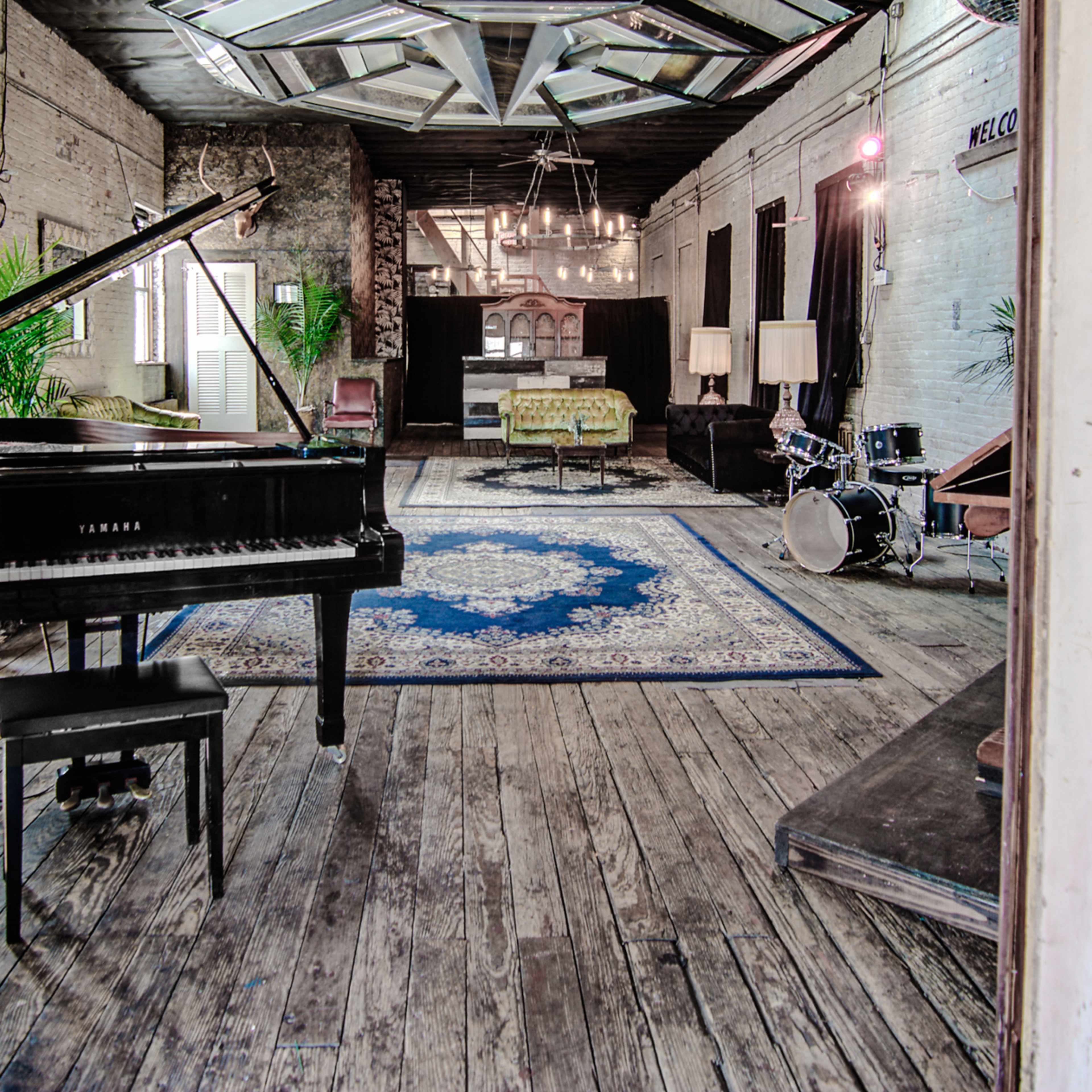 A spacious room with a grand piano, a rug, a seating area, and various musical instruments arranged on a wooden floor.